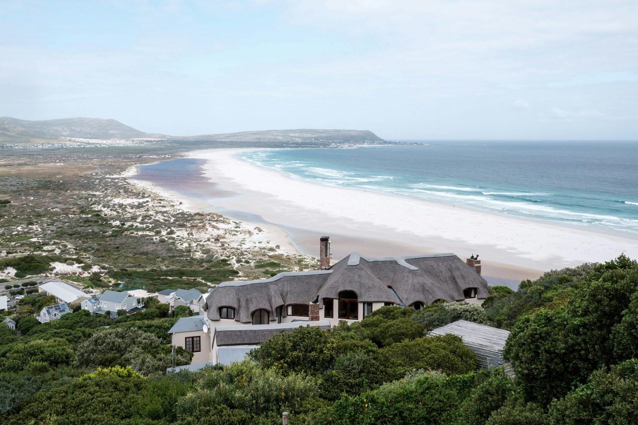 Casa moderna con tejado de paja que domina una amplia playa de arena blanca y el océano turquesa en Sudáfrica