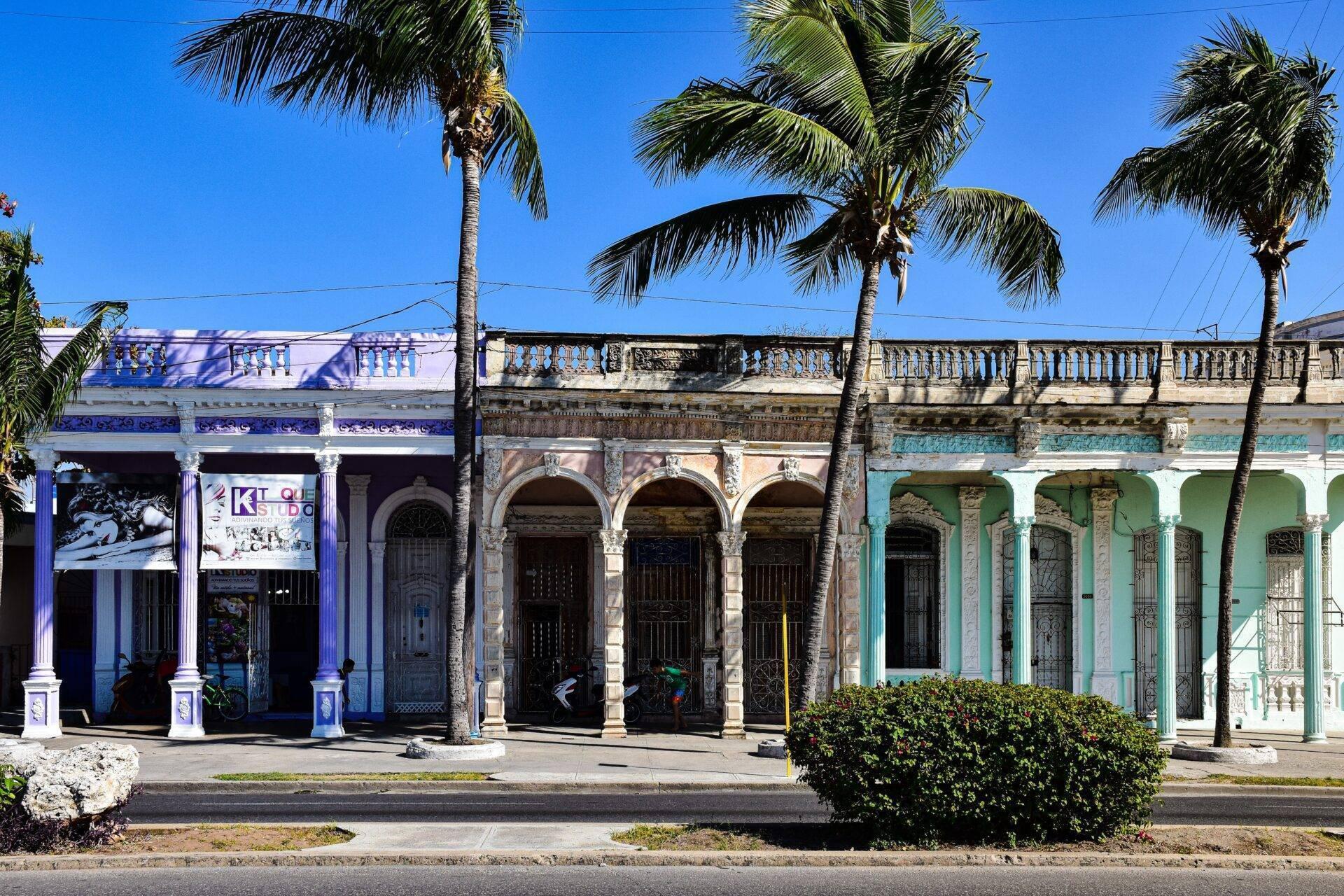 Facciate colorate di edifici coloniali con arcate, palme e balaustre ornamentali sotto un cielo blu