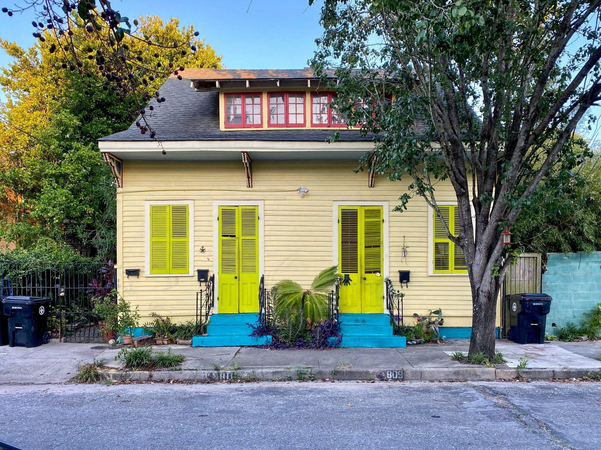 Casa colorata con porte e persiane giallo brillante, base blu e finestre rosse al piano superiore, circondata da vegetazione