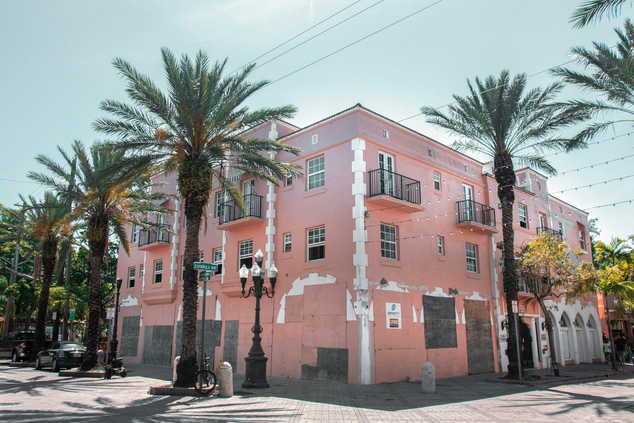 A pink colonial building with white columns, palm trees and a vintage street lamp on a sunny cobbled street