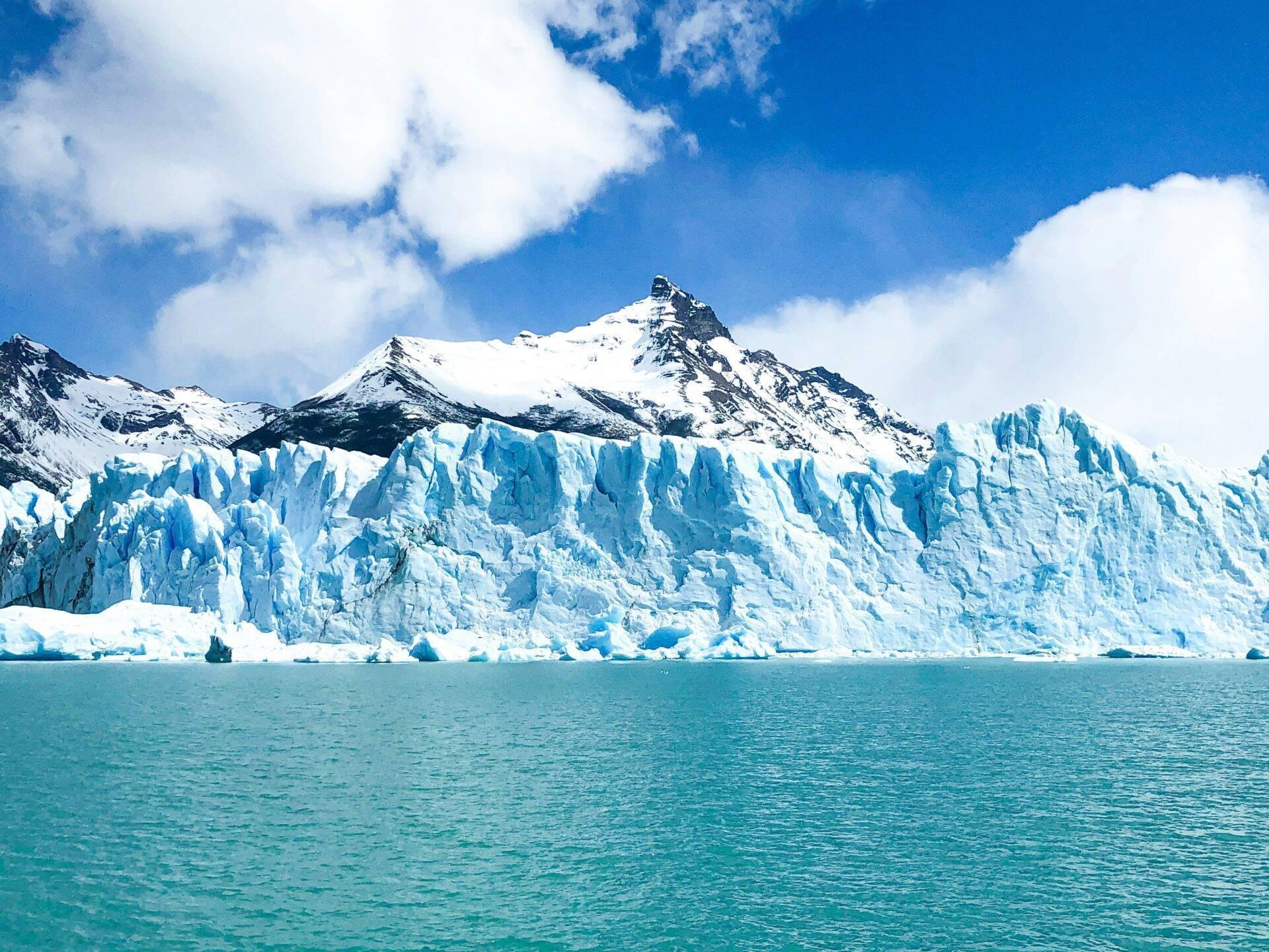 Un massiccio ghiacciaio azzurro con le sue caratteristiche formazioni di ghiaccio di fronte a una montagna innevata sotto un cielo sereno