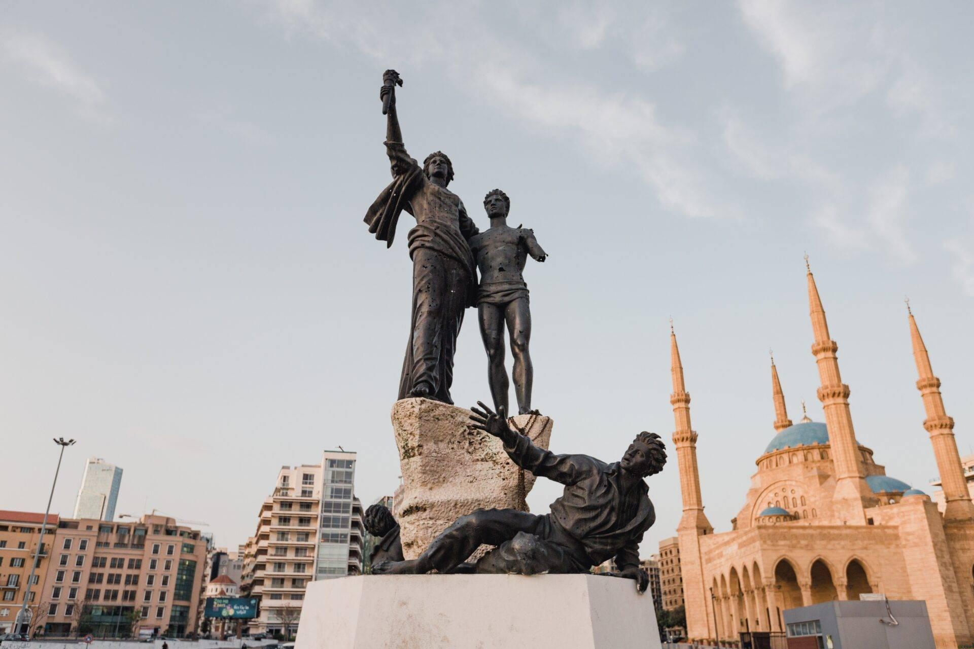Monumento de bronce con figuras en lucha y una mezquita dorada al fondo en una plaza urbana