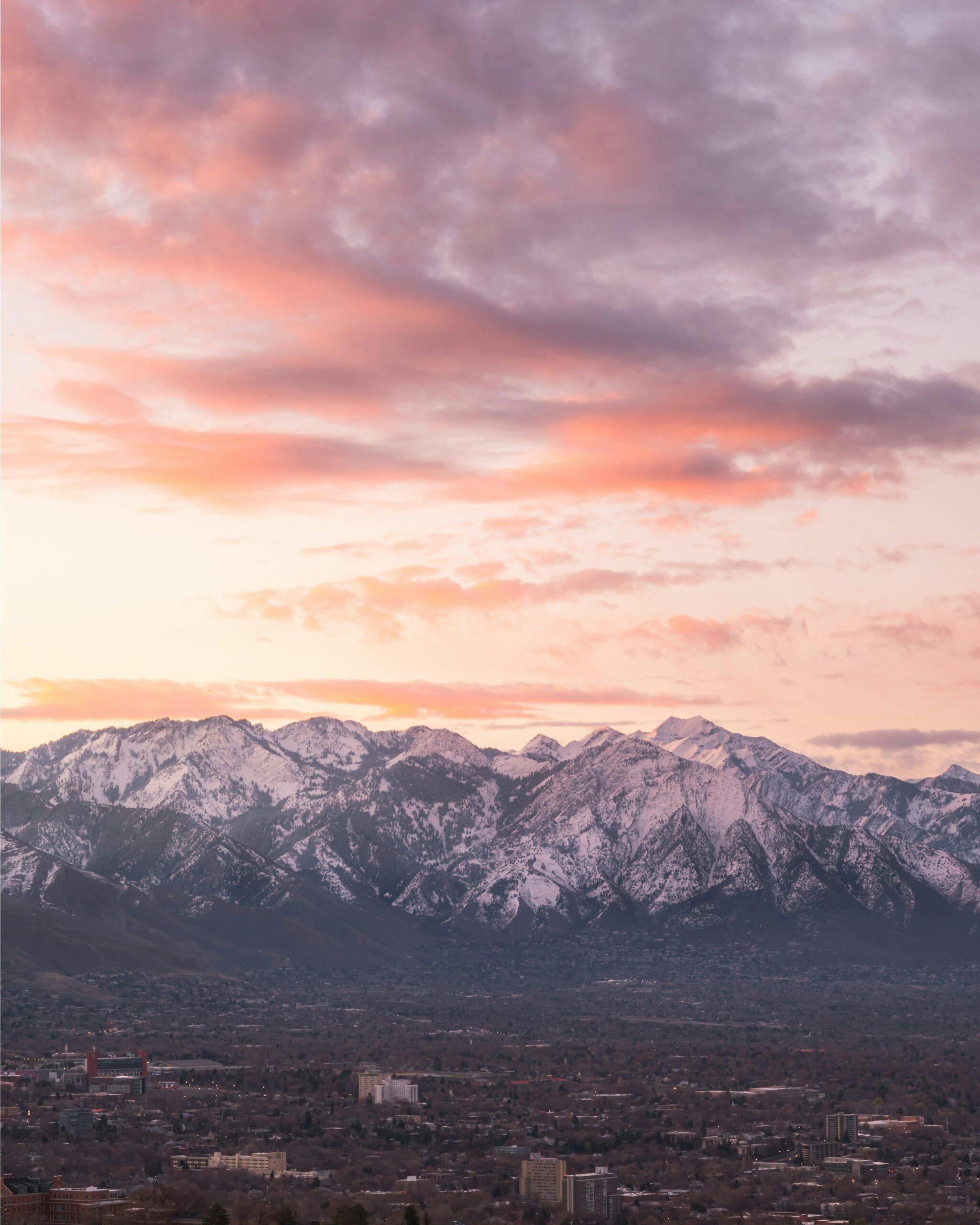 Panoramablick auf eine Gebirgsstadt im Sonnenuntergang mit verschneiter Bergkette im Hintergrund