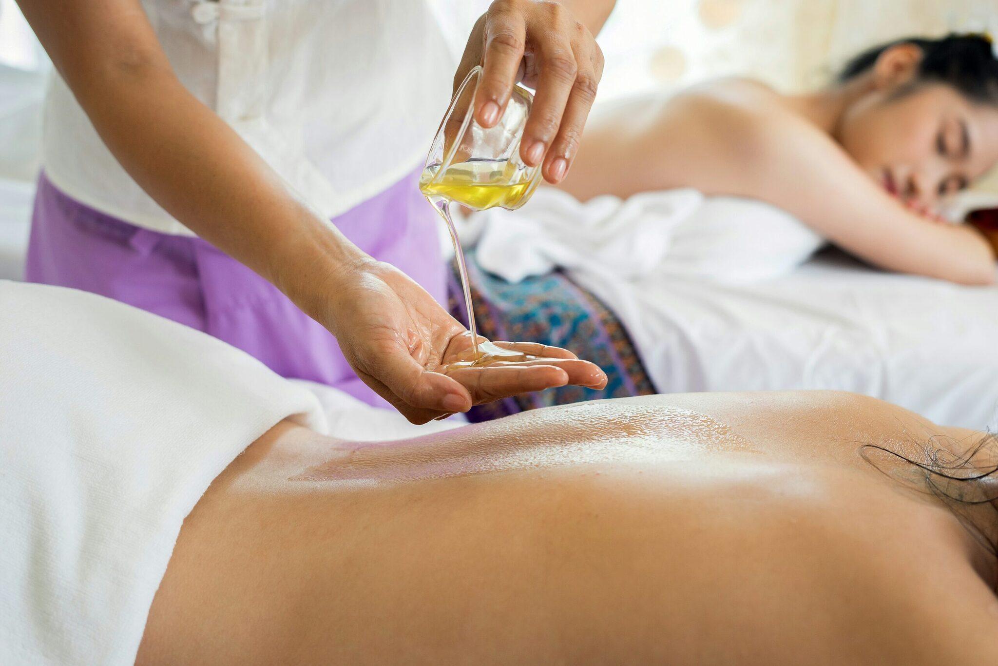 Eine Therapeutin träufelt Massageöl auf den Rücken einer liegenden Kundin in einem Spa