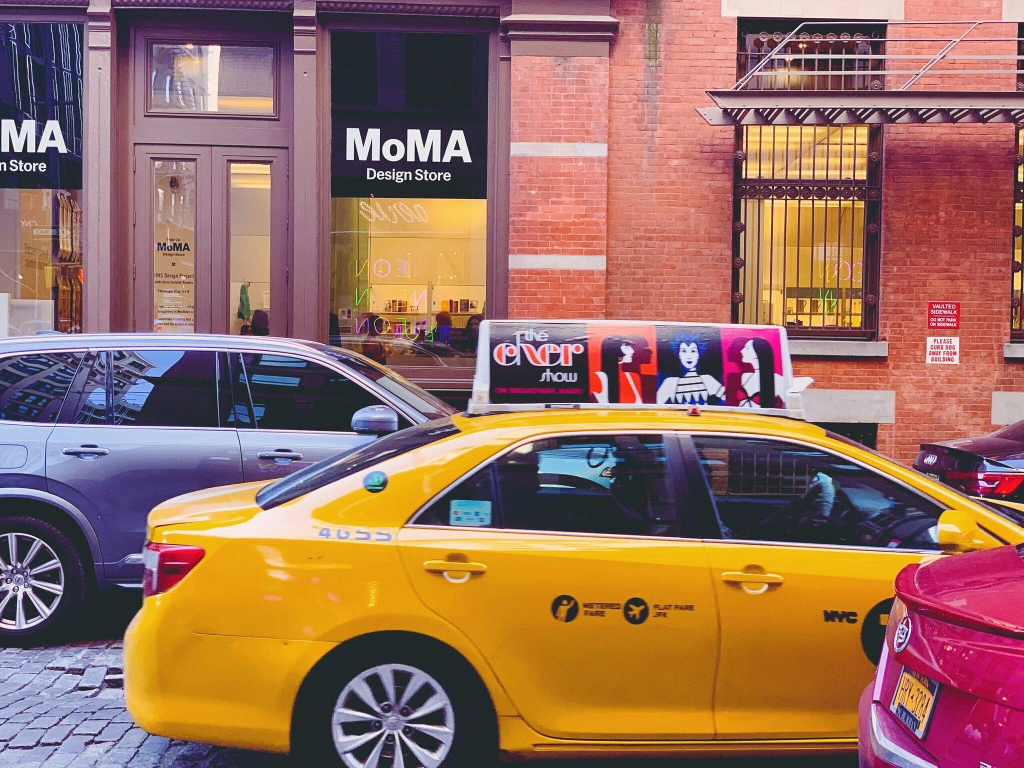 A busy urban shopping street with yellow taxis, modern shop fronts and red-brick architecture