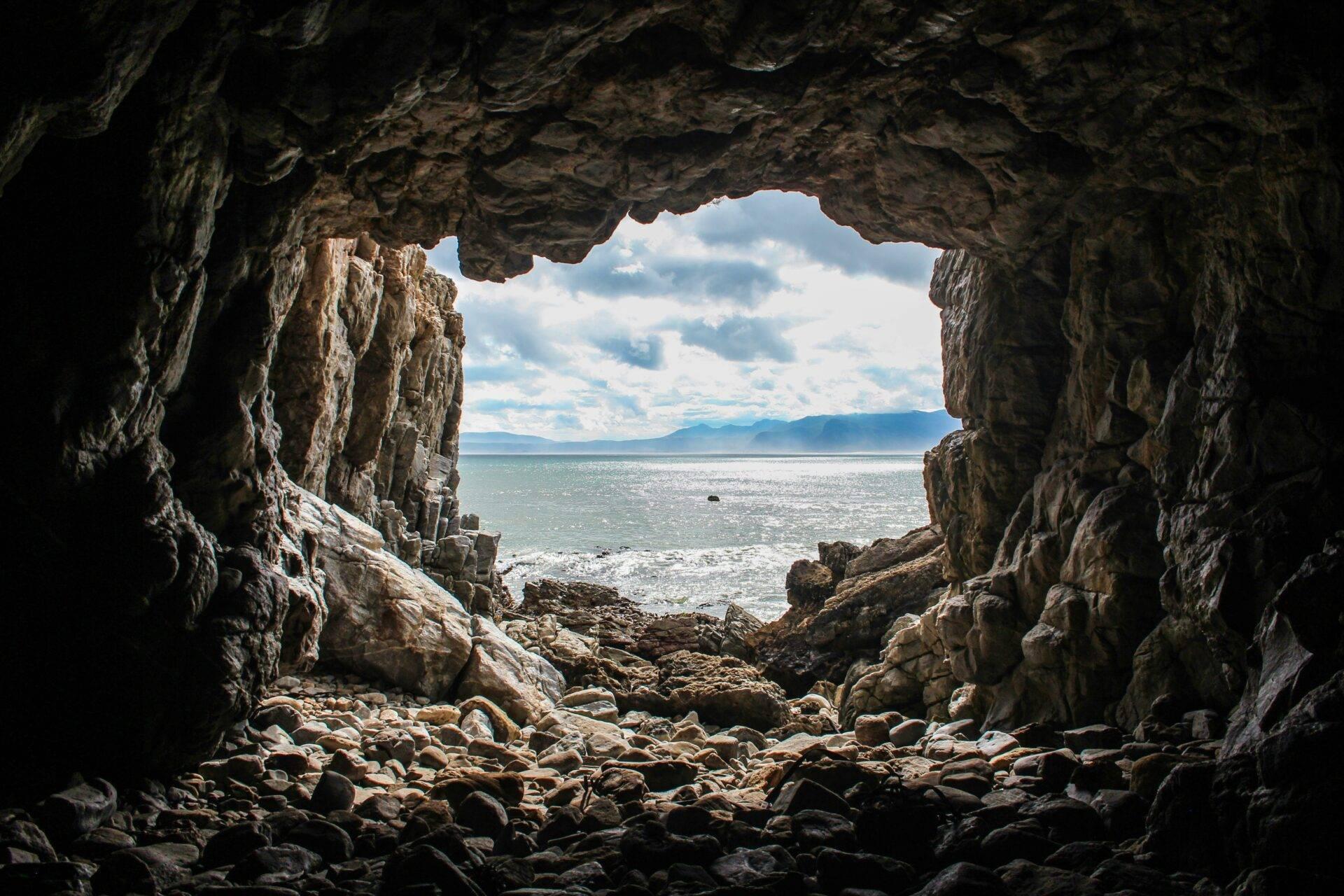 Vista desde el interior de una cueva costera sobre el mar, las montañas y un cielo nublado
