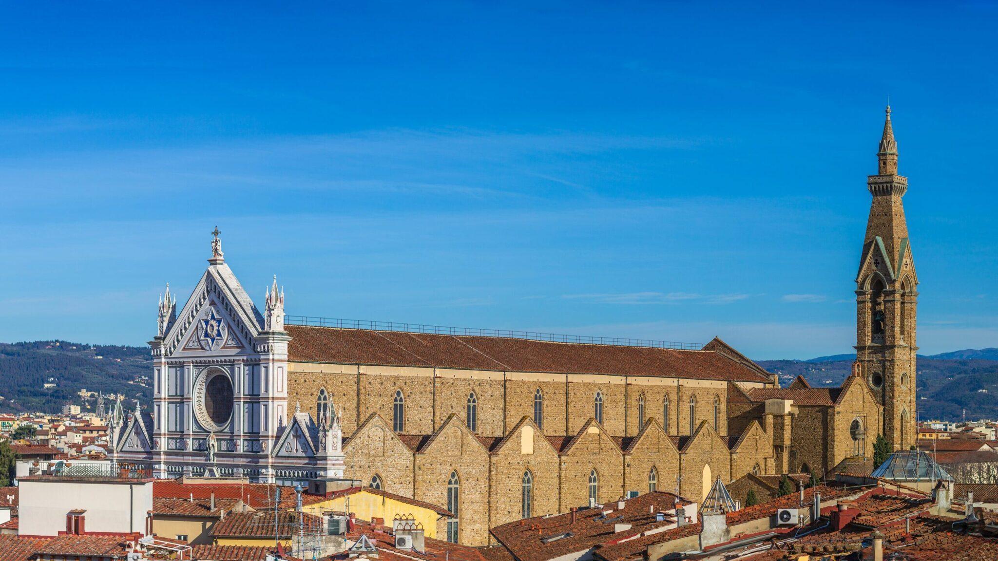 Vista panorámica de Florencia con una basílica de piedra ocre, un esbelto campanile y la cúpula blanca de una catedral bajo cielo azul