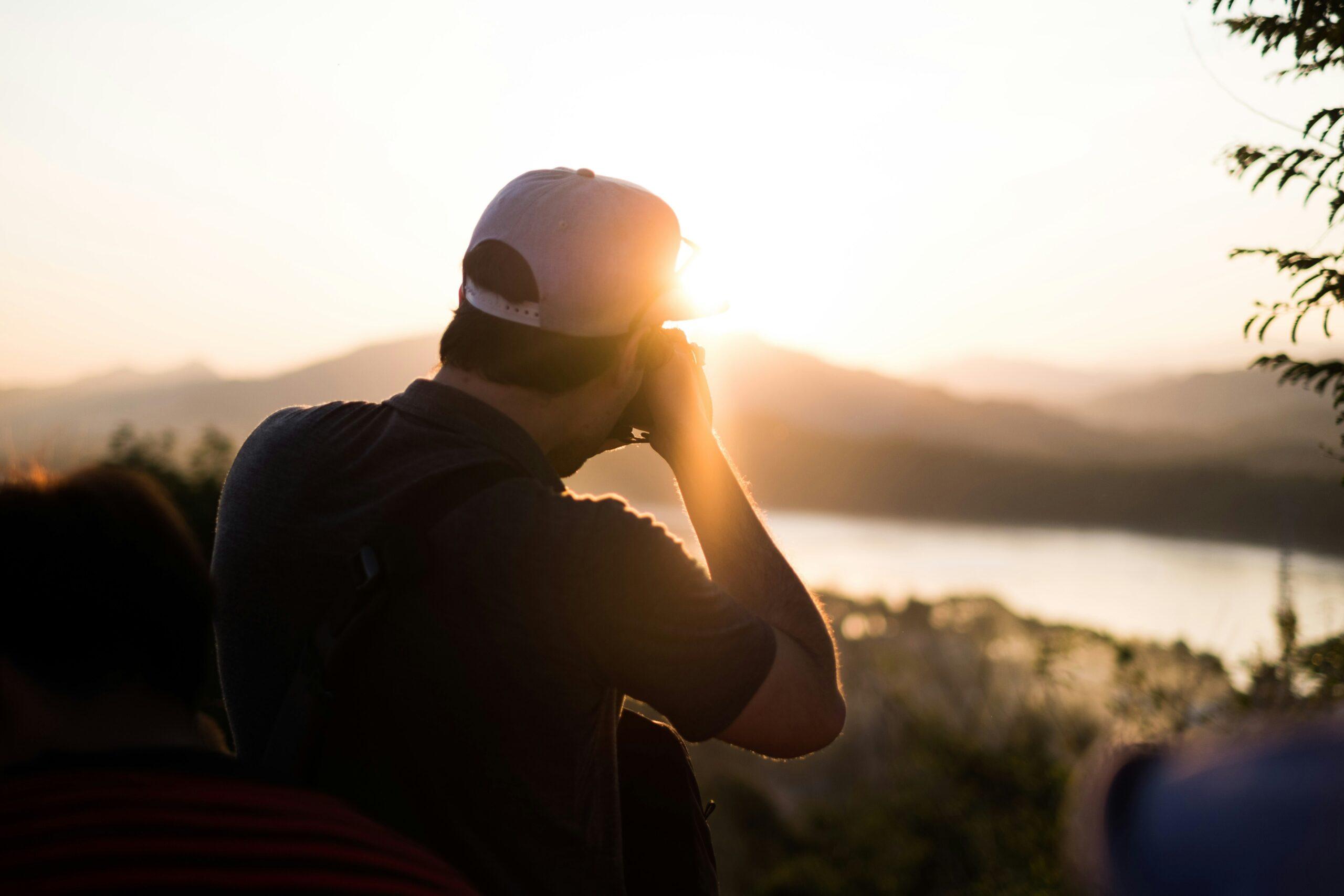 Mann beim Sonnenuntergang mit Blick auf eine Berglandschaft mit See von einem Aussichtspunkt aus
