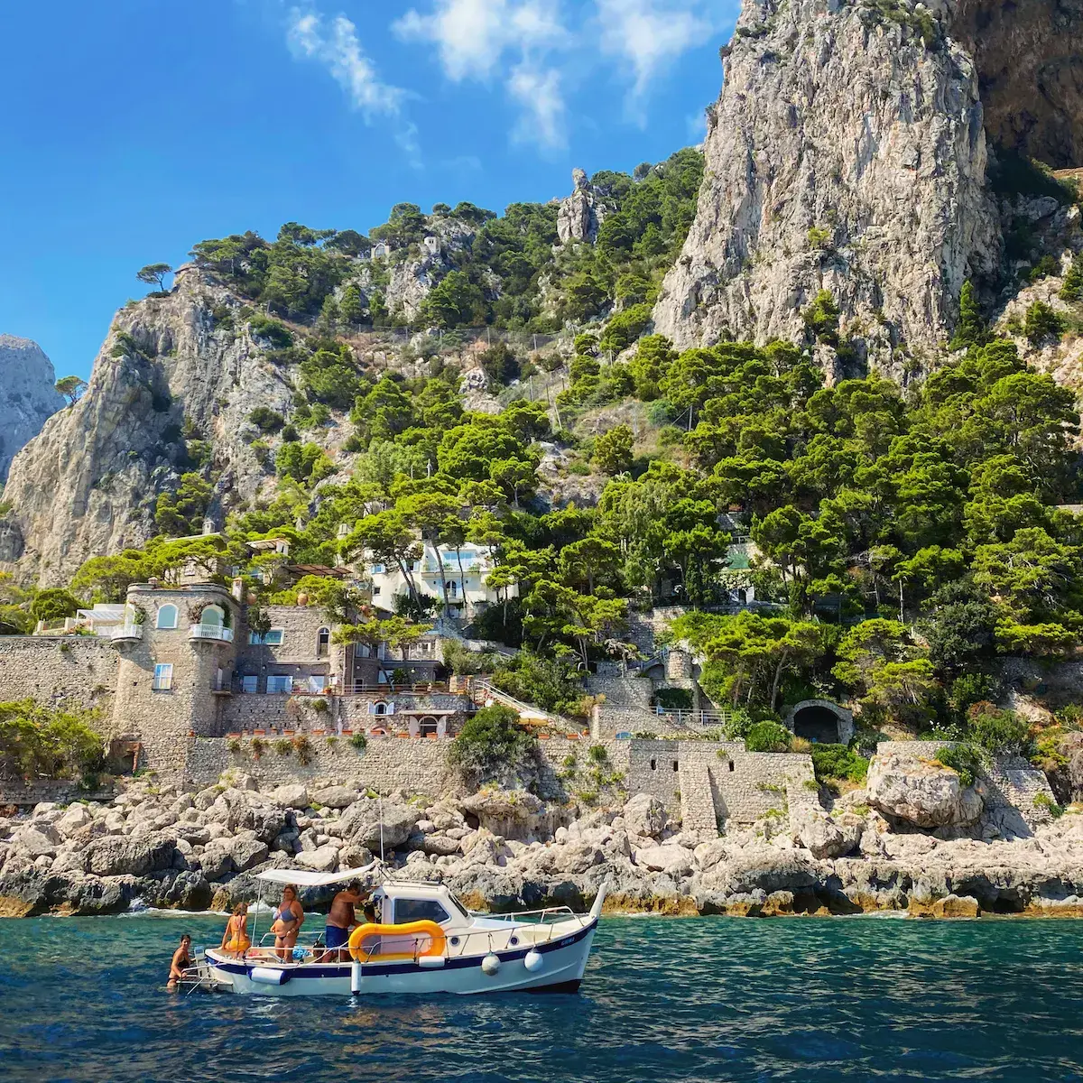 Ein blau-weißes Fischerboot vor Steinhäusern, die an eine mediterrane Felswand geschmiegt sind