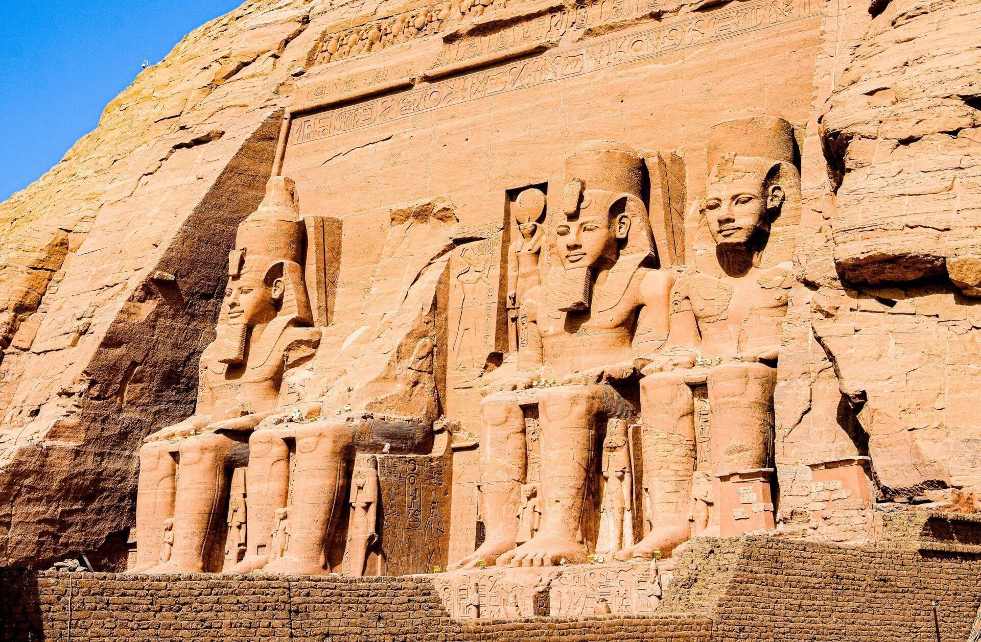 Facciata rocciosa di un antico tempio egizio con quattro colossi scolpiti e geroglifici sotto un cielo azzurro