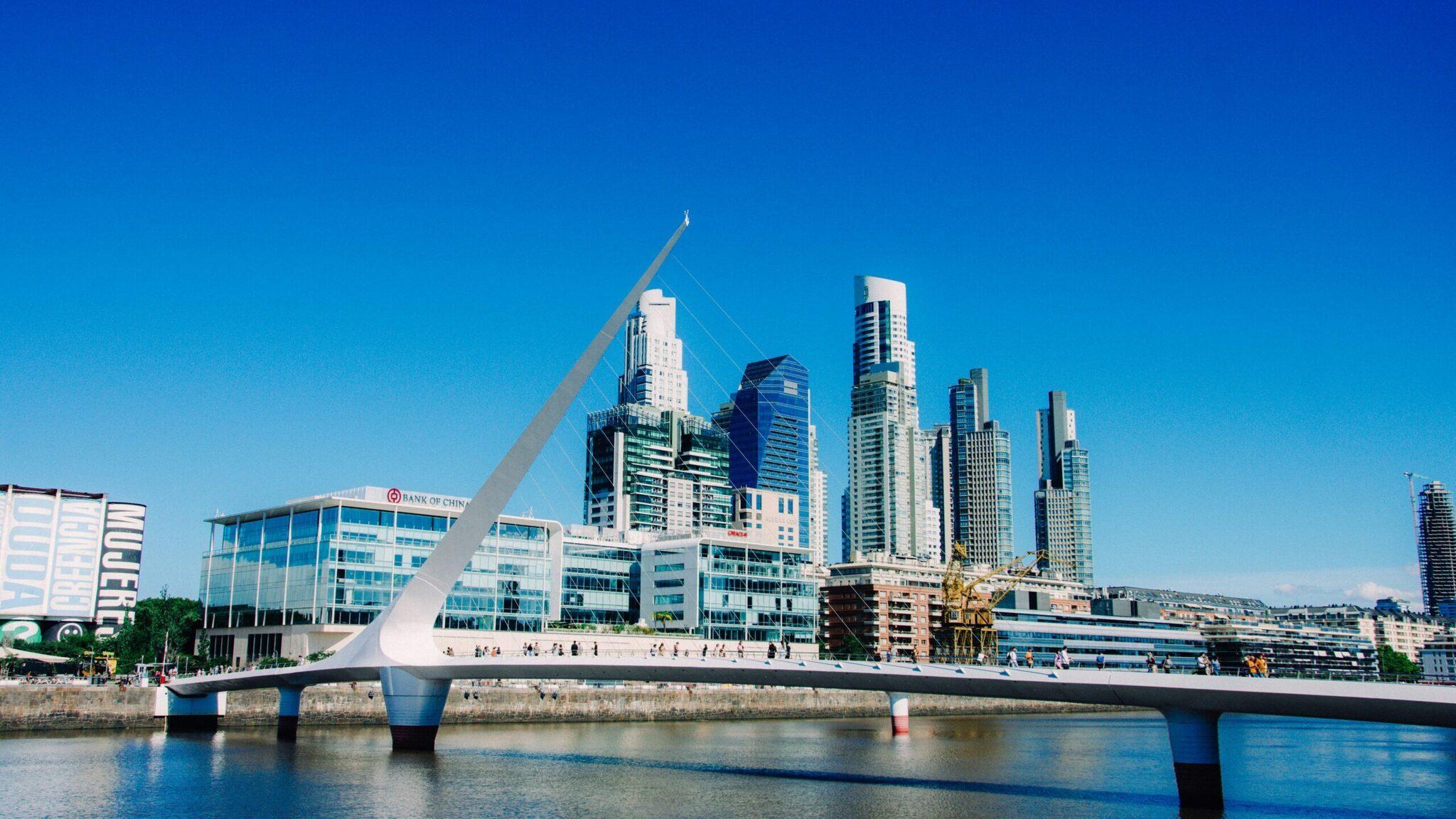 Un ponte bianco moderno che scavalca un canale con grattacieli contemporanei sullo sfondo e cielo azzurro