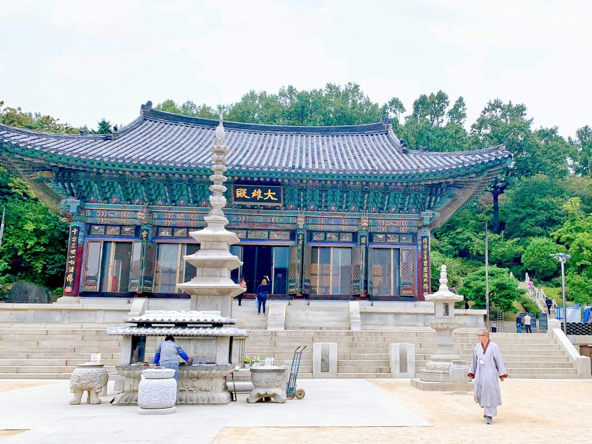 Koreanischer buddhistischer Tempel mit blauem und grünem traditionellen Dach, Steinpagode und Besuchern auf einem gepflasterten Innenhof