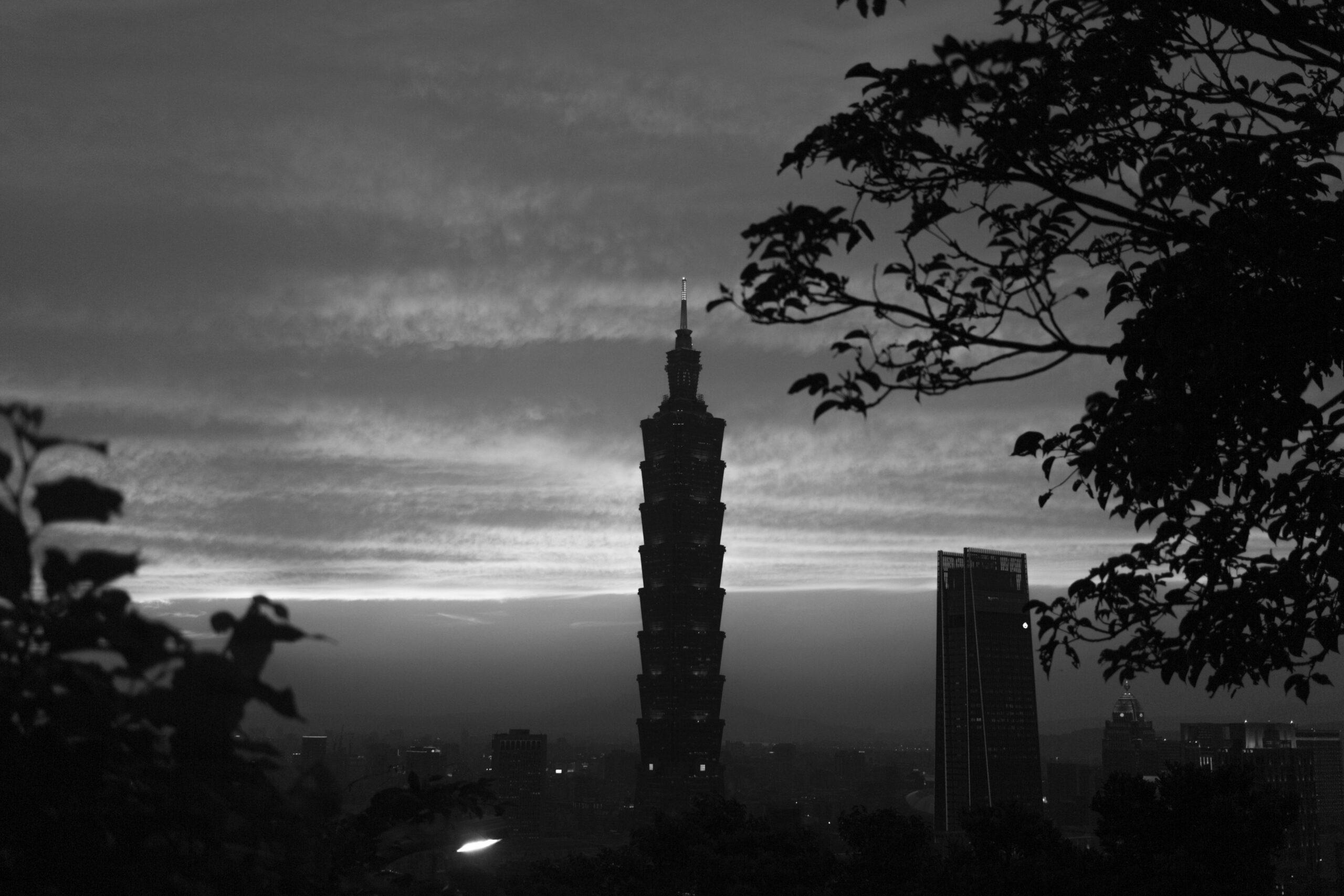 Vista panorámica al atardecer de una esbelta torre dominante rodeada de edificios modernos y enmarcada por vegetación