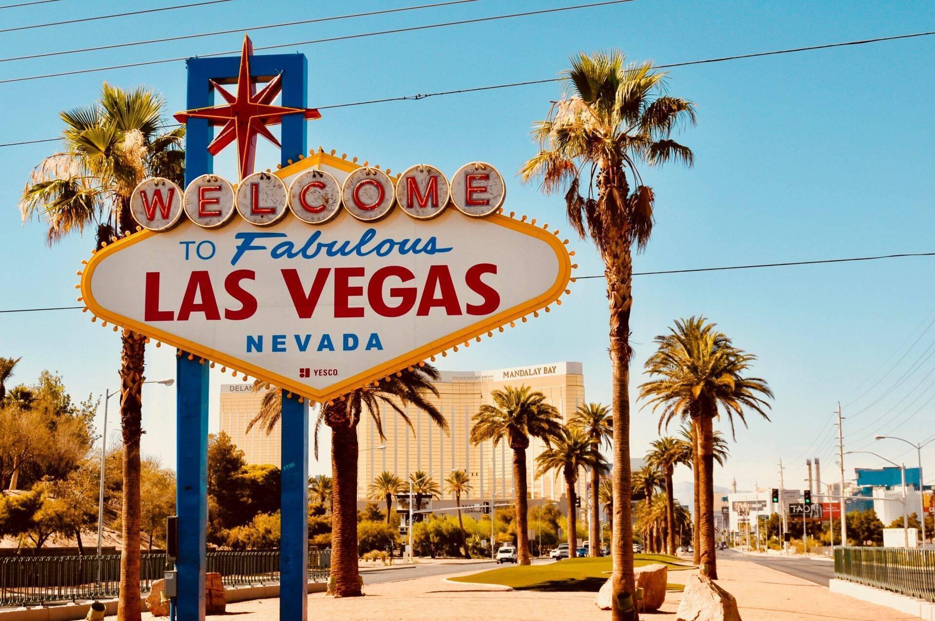 Das berühmte Willkommensschild von Las Vegas mit Palmen und Kasinos im Hintergrund unter blauem Himmel