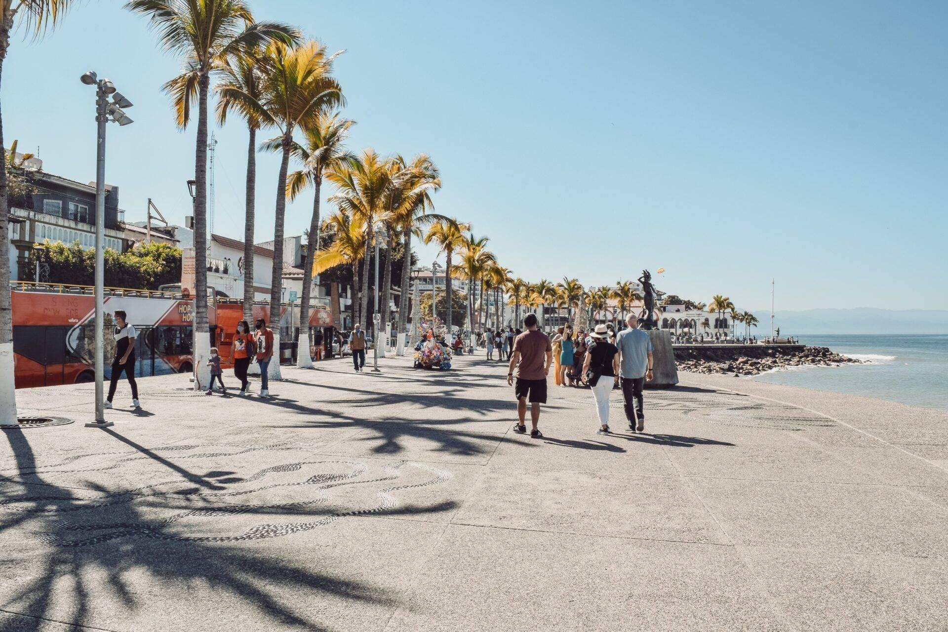 Belebte Küstenpromenade mit Palmen, Kolonialgebäuden und Blick aufs Meer