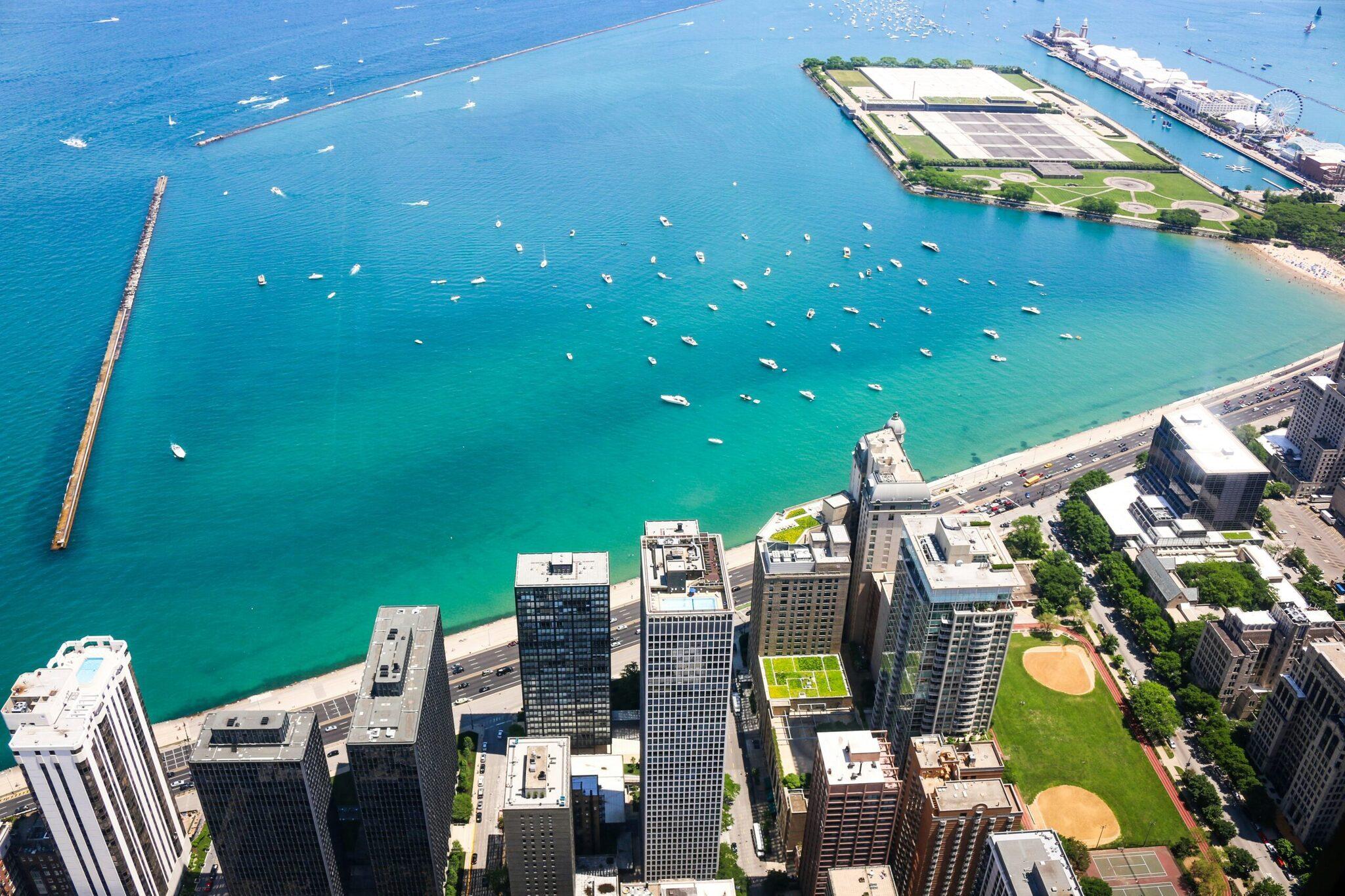Luftaufnahme von Chicagos Uferpromenade mit Wolkenkratzern, Sandstrand, türkisblauem See und vertäuten Freizeitbooten