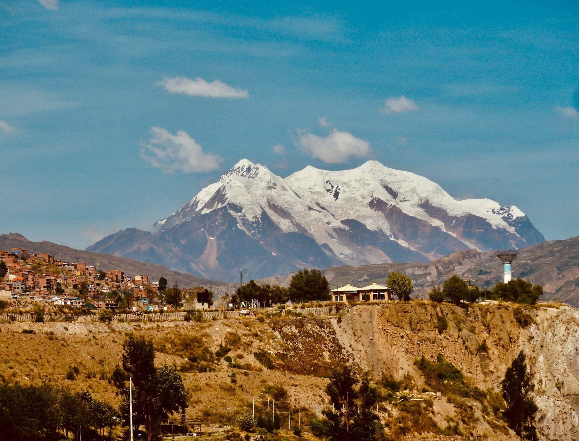 Città andina di montagna con case in adobe e maestoso vulcano innevato sullo sfondo sotto un cielo azzurro