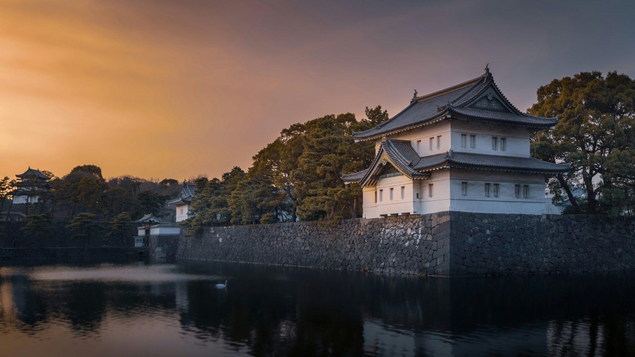 Un castillo japonés blanco de tejados en pagoda reflejado en un estanque tranquilo al atardecer, rodeado de vegetación