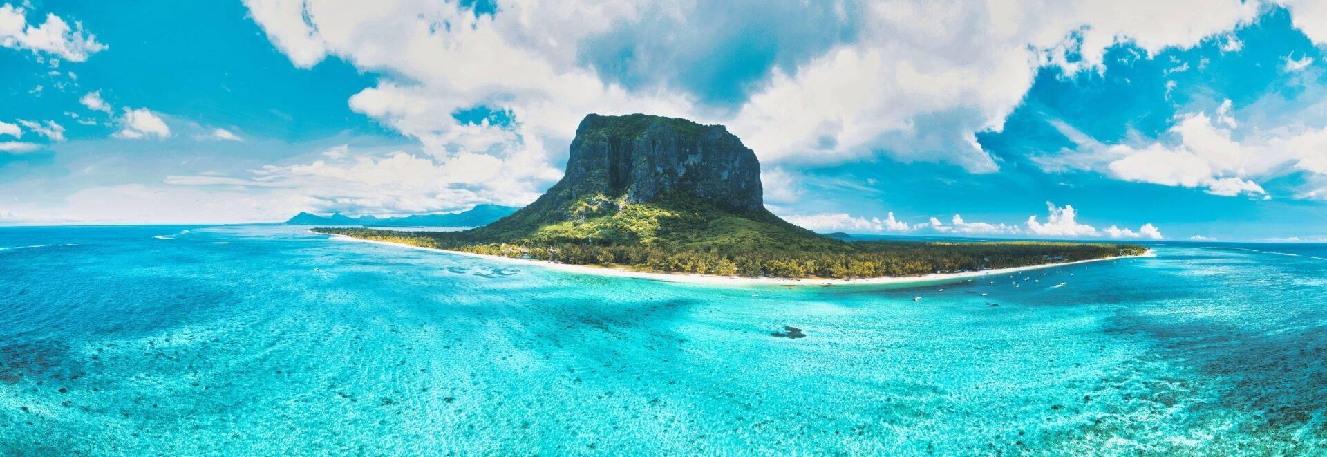 Una isla tropical de acantilados verdes rodeada de agua turquesa cristalina bajo un cielo azul nublado