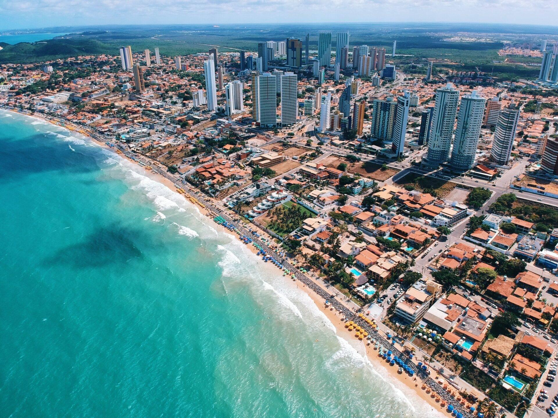 Vista aerea di una località balneare costiera con spiaggia turchese, grattacieli moderni e residenze colorate sul mare
