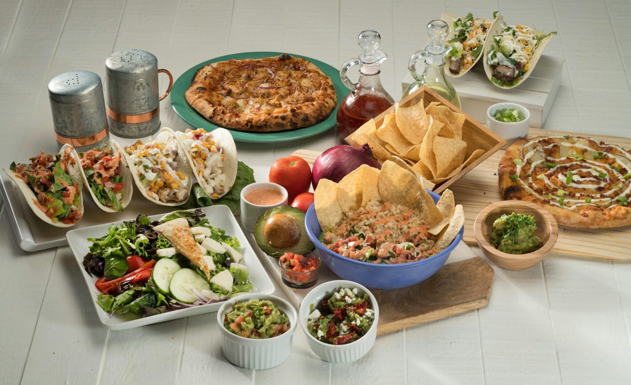 Ein weißer Küchentisch mit einer Auswahl mexikanischer Gerichte: Tacos, Nachos, Ceviche und frische Salate