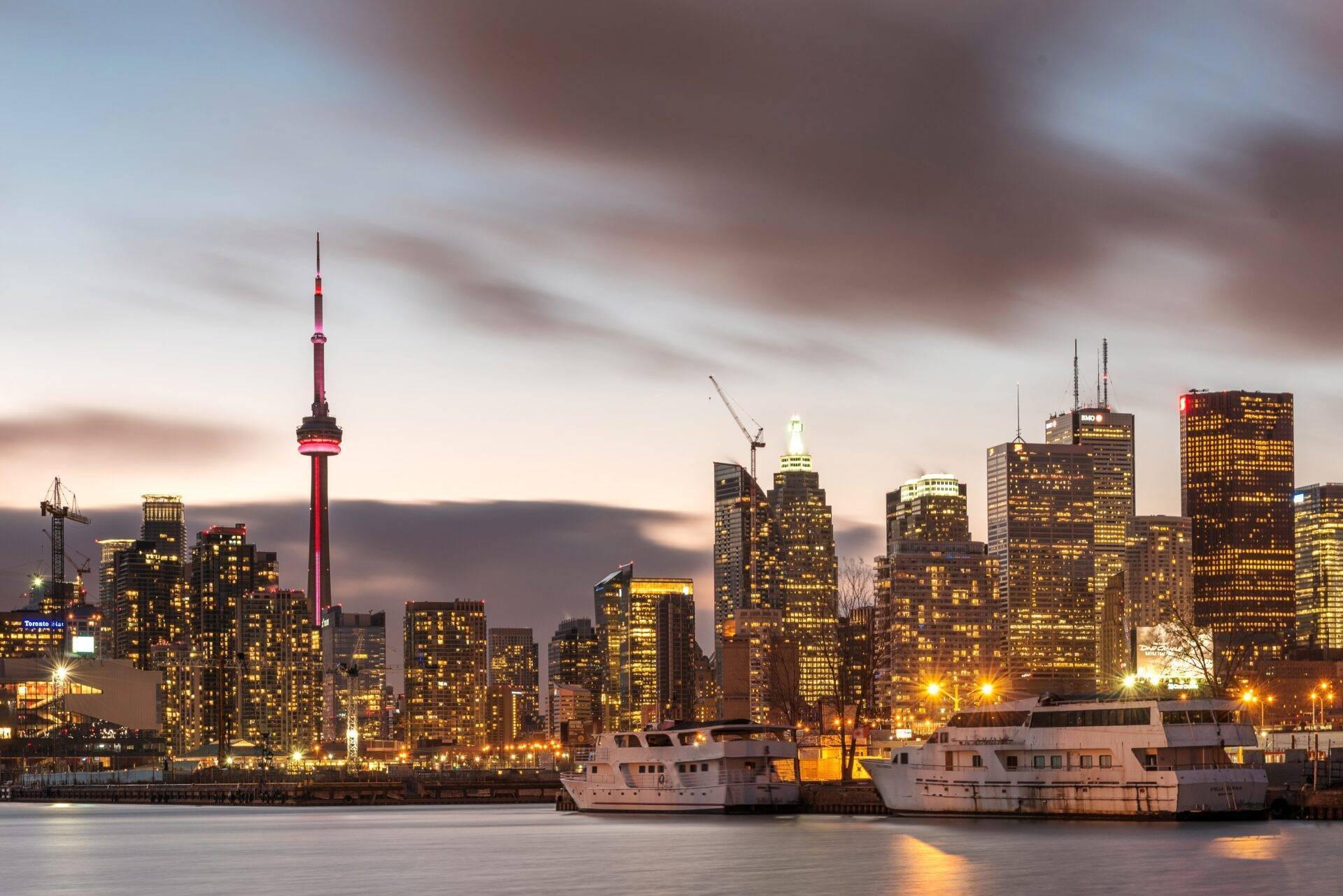 Städtische Skyline in der Abenddämmerung mit beleuchteten Wolkenkratzern, markantem Fernsehturm und im Hafen liegenden Booten