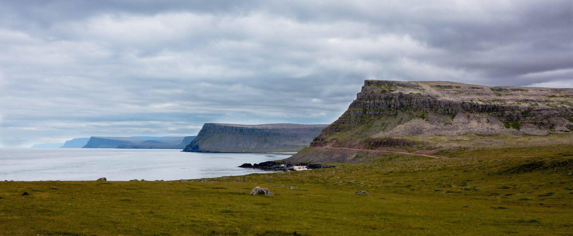Acantilados basálticos verdes que dominan una bahía tranquila con formaciones rocosas características del paisaje islandés