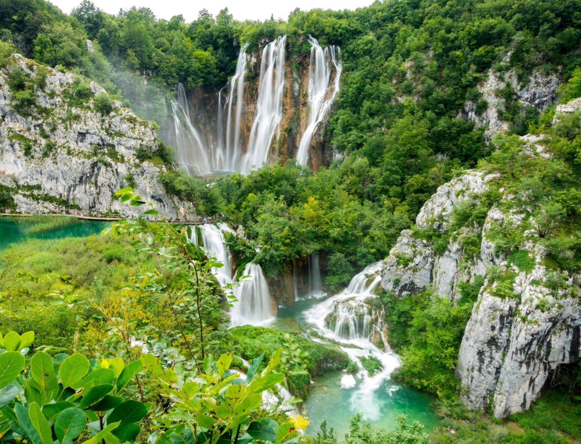 Cascate spettacolari che scendono su pareti calcaree in una gola boscosa con laghi turchesi