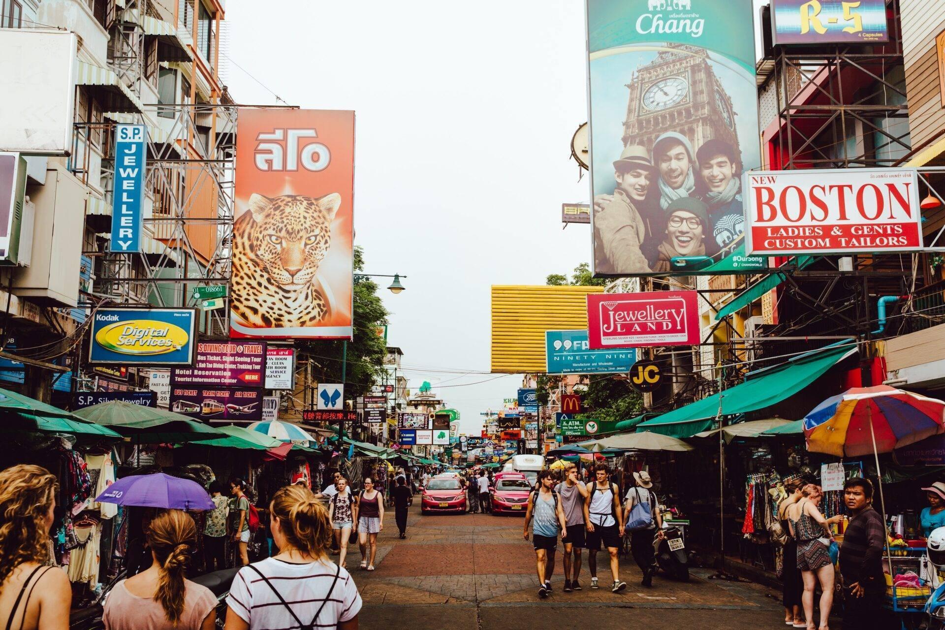 Una vivace strada commerciale di Bangkok con bancarelle, insegne colorate e una folla di turisti e residenti