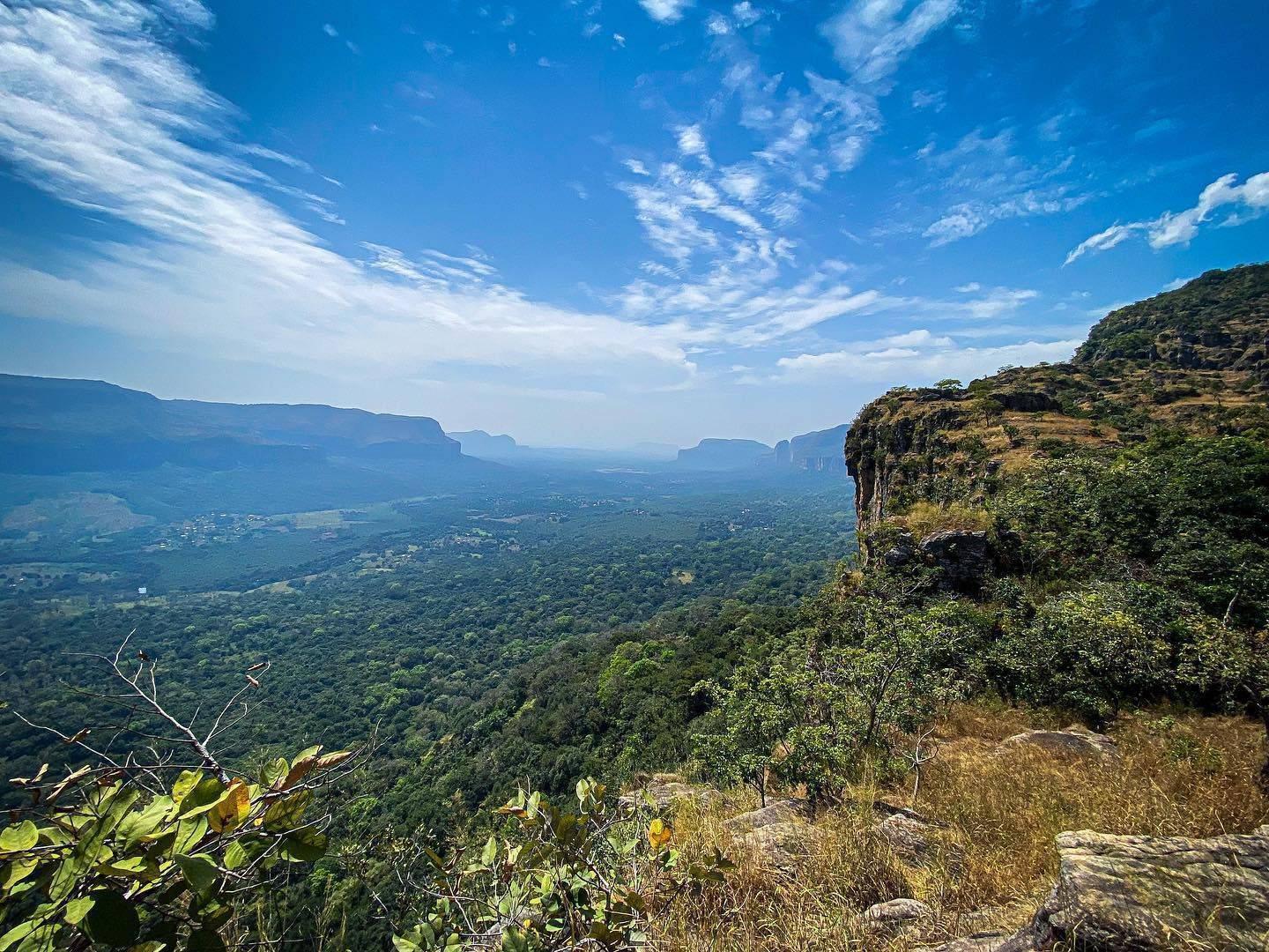 Vista panoramica da un altipiano roccioso su una vallata verdeggiante con formazioni montuose sullo sfondo sotto un cielo azzurro