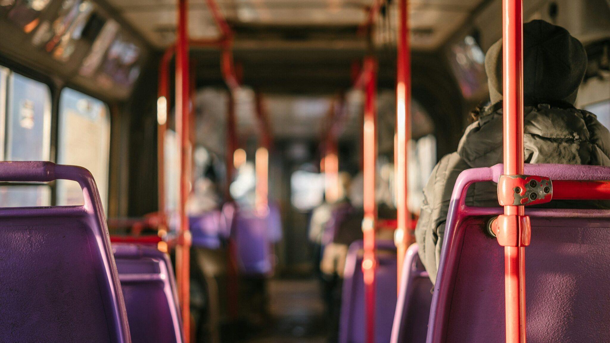 Innenraum eines öffentlichen Busses mit violetten Sitzen und roten Haltestangen