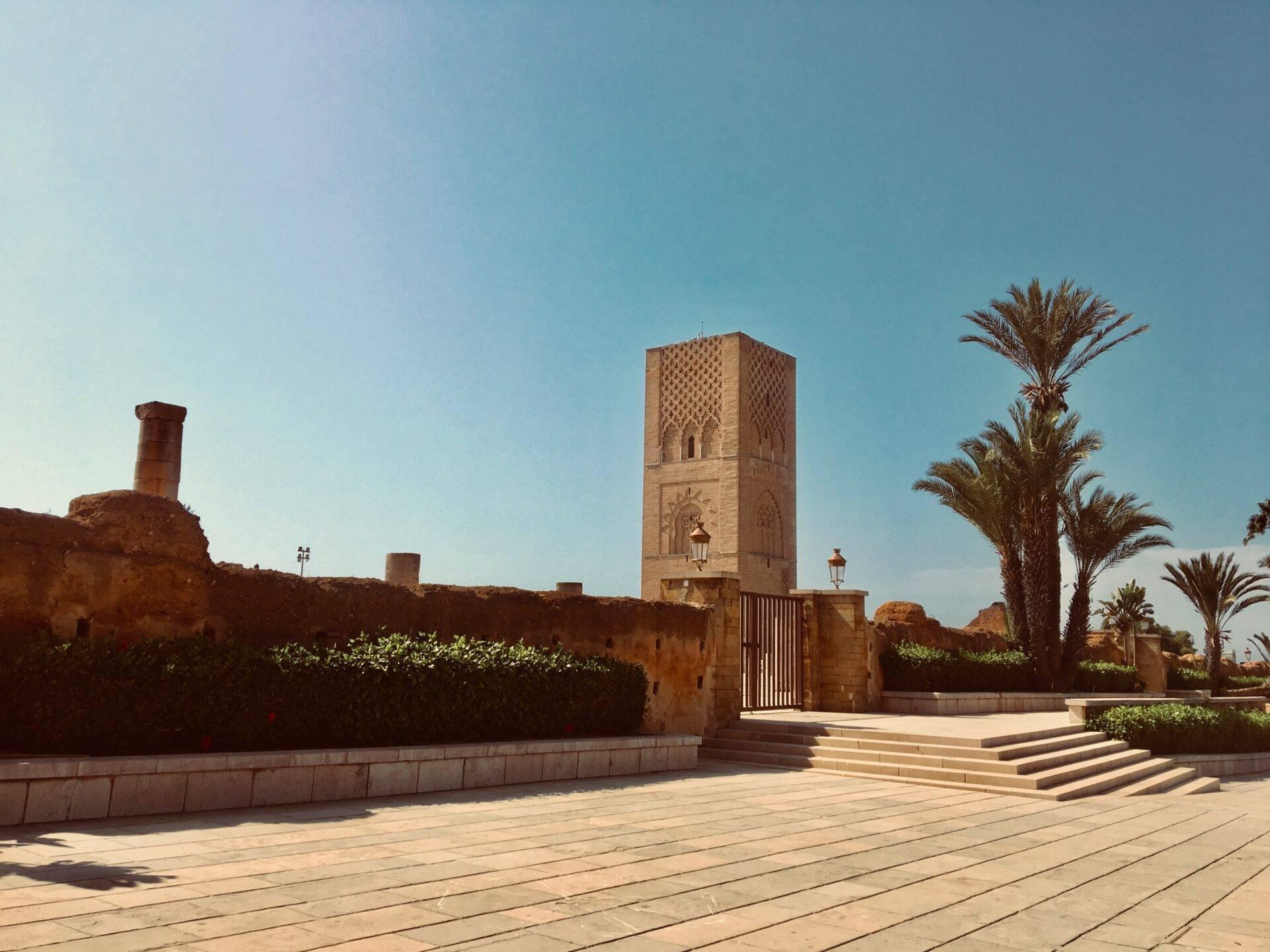 Traditionelle marokkanische Moschee mit Terrakotta-Minarett, gepflasterter Terrasse und Palmen unter blauem Himmel