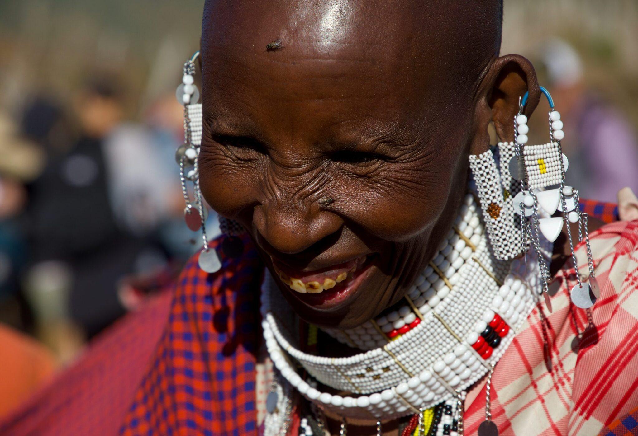 Mujer sonriente con ropa tradicional de colores vivos y abalorios blancos característicos de la cultura africana