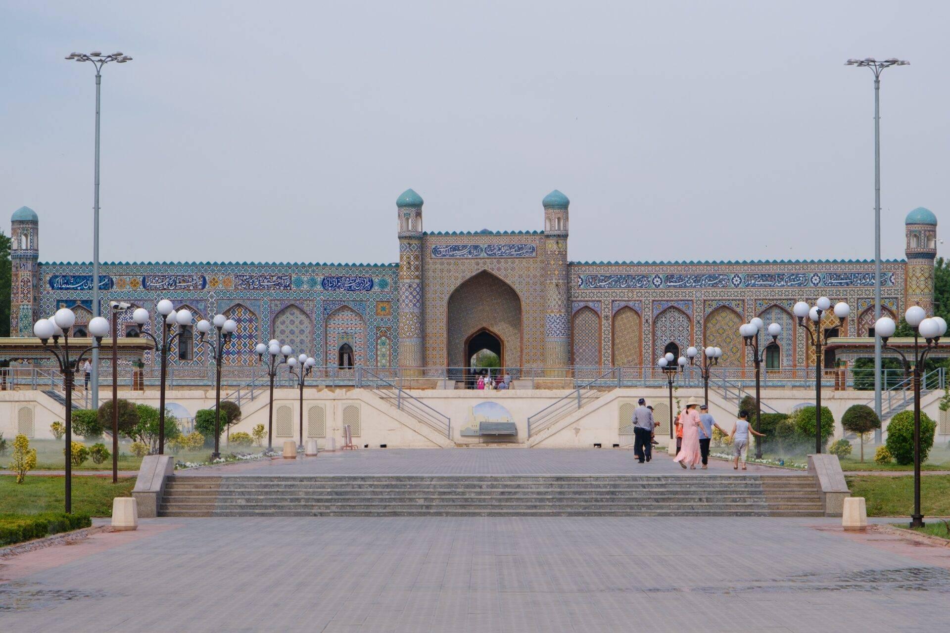 Große Moschee mit blau-goldener Schmuckfassade, zentralem Minarett, gepflastertem Hof und Besuchern in leichter Kleidung