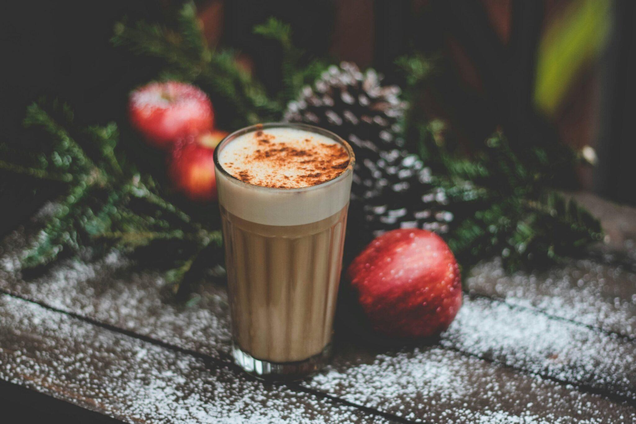 Un cappuccino decorado con cacao sobre una superficie invernal rodeada de adornos navideños