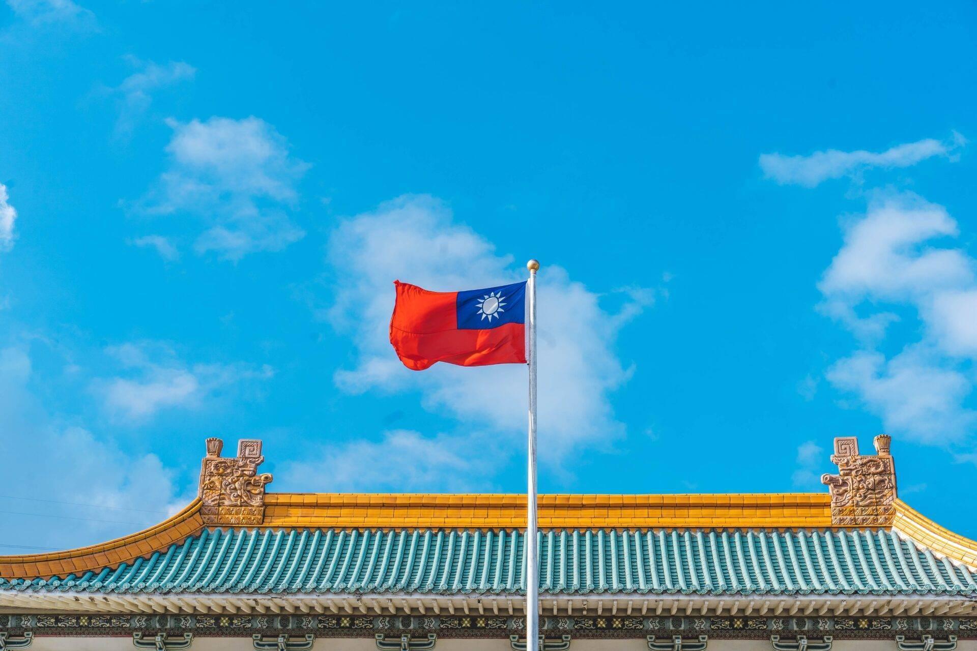 La bandiera di Taiwan sventola davanti a un tempio tradizionale con tetti dorati e turchesi sotto un cielo azzurro