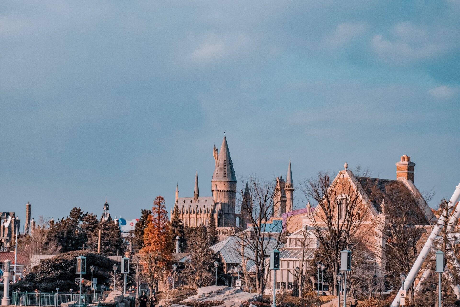 Ein Schloss im gotischen Stil mit spitzen Türmen, umgeben von bunten Gebäuden und herbstlichen Bäumen unter klarem Himmel