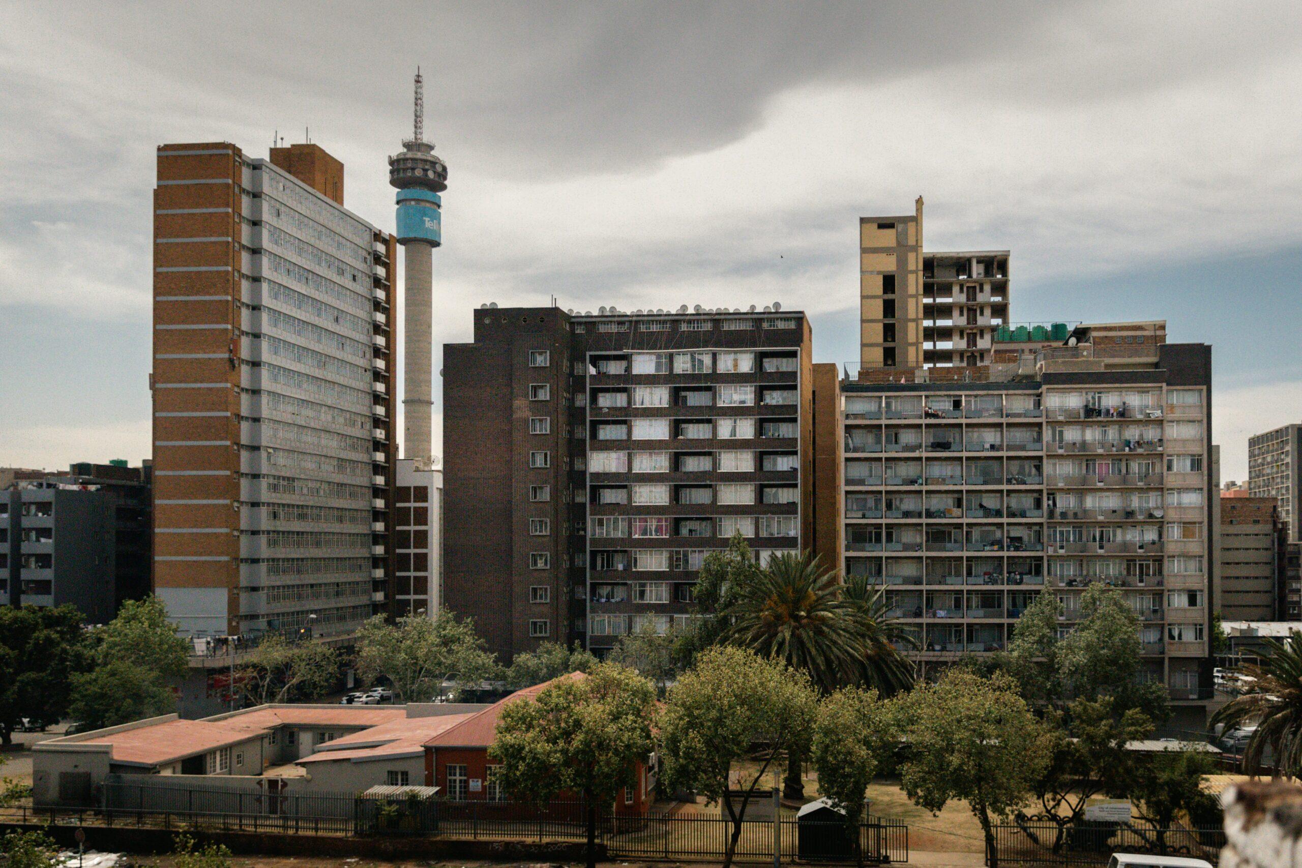 Skyline urbano con edificio de ladrillo rojo, torre de telecomunicaciones azul y edificios residenciales bajo cielo nublado