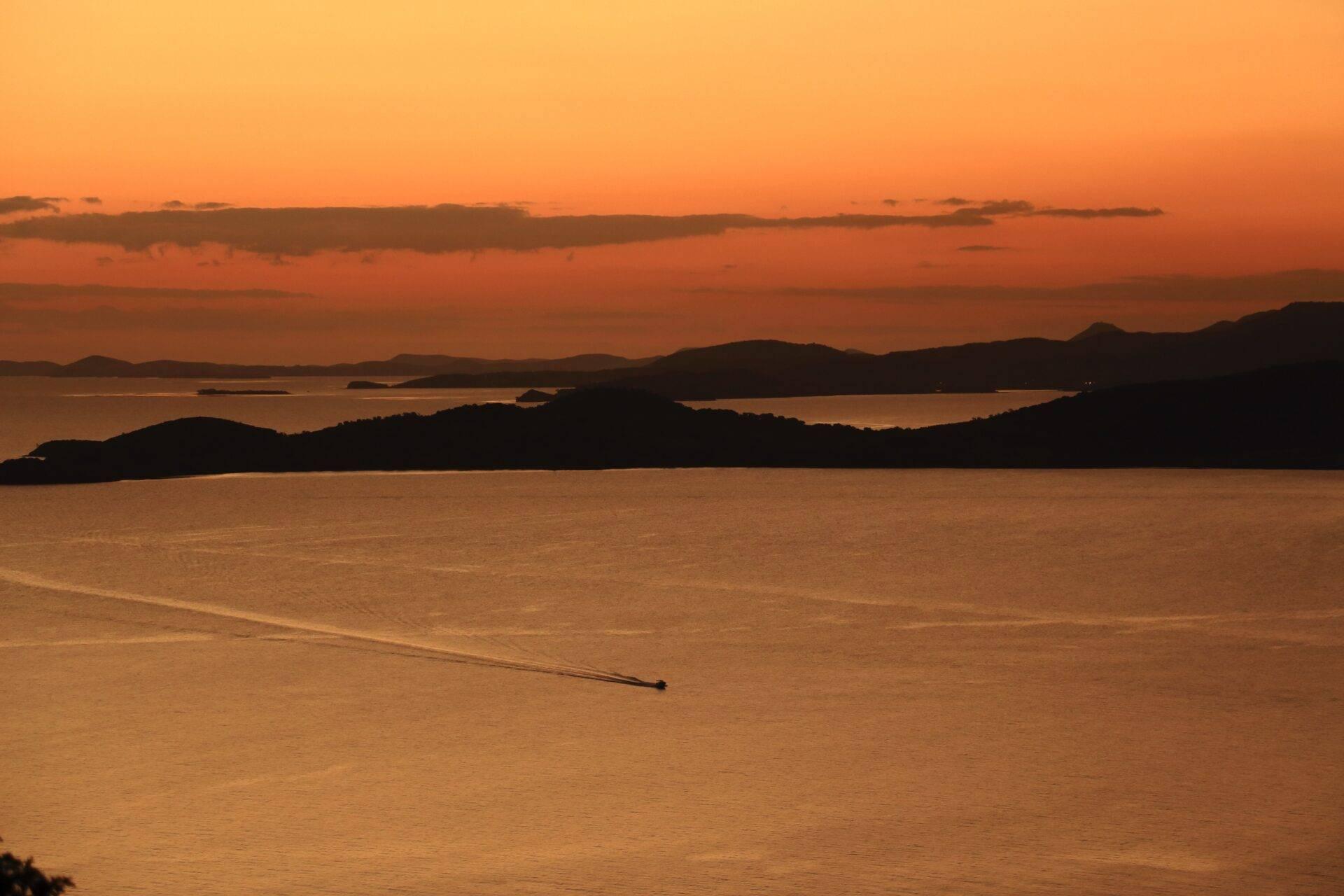 Goldener Sonnenuntergang über einer Tropenbucht mit bewaldeten Inseln und einem kleinen Boot auf dem offenen Wasser