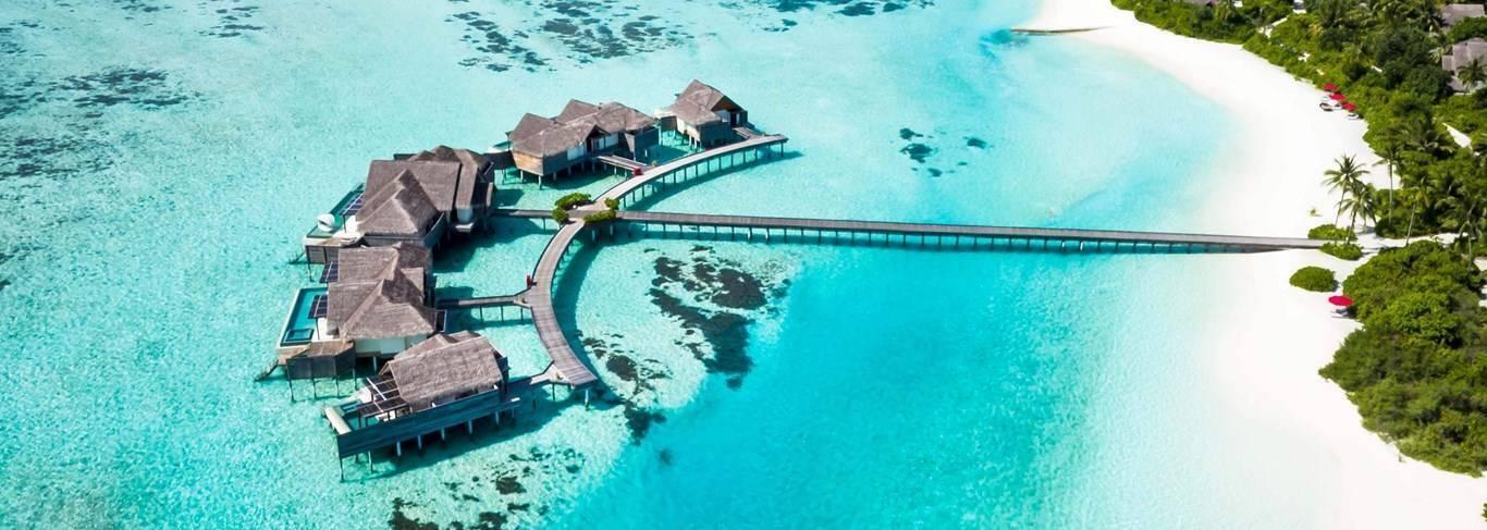 Vista aerea di un resort tropicale con bungalow sull’acqua, spiaggia di sabbia bianca e laguna turchese cristallina