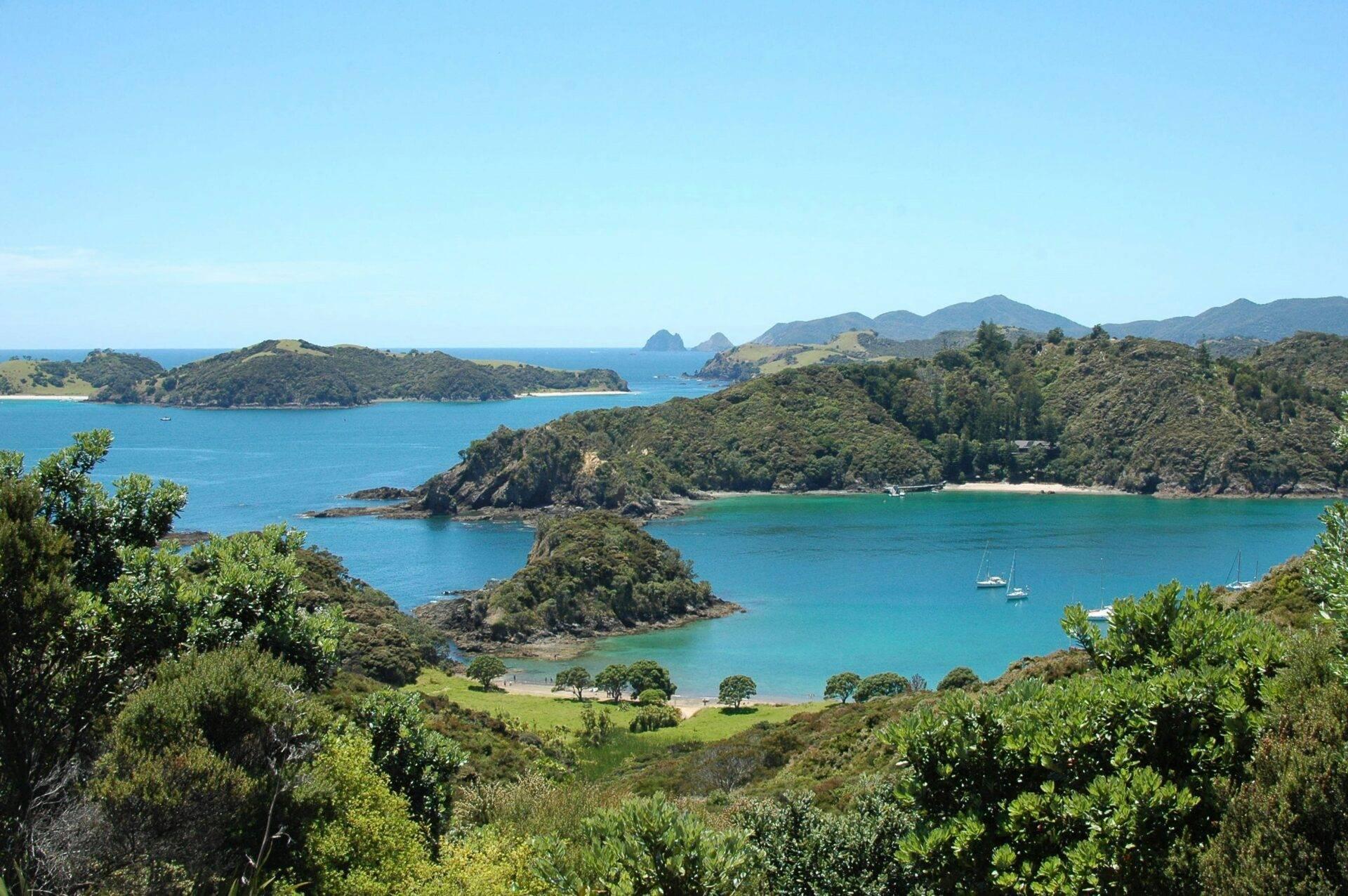 Vista panoramica di una baia costiera con isole boscose, spiagge turchesi e barche a vela ancorate in acque cristalline
