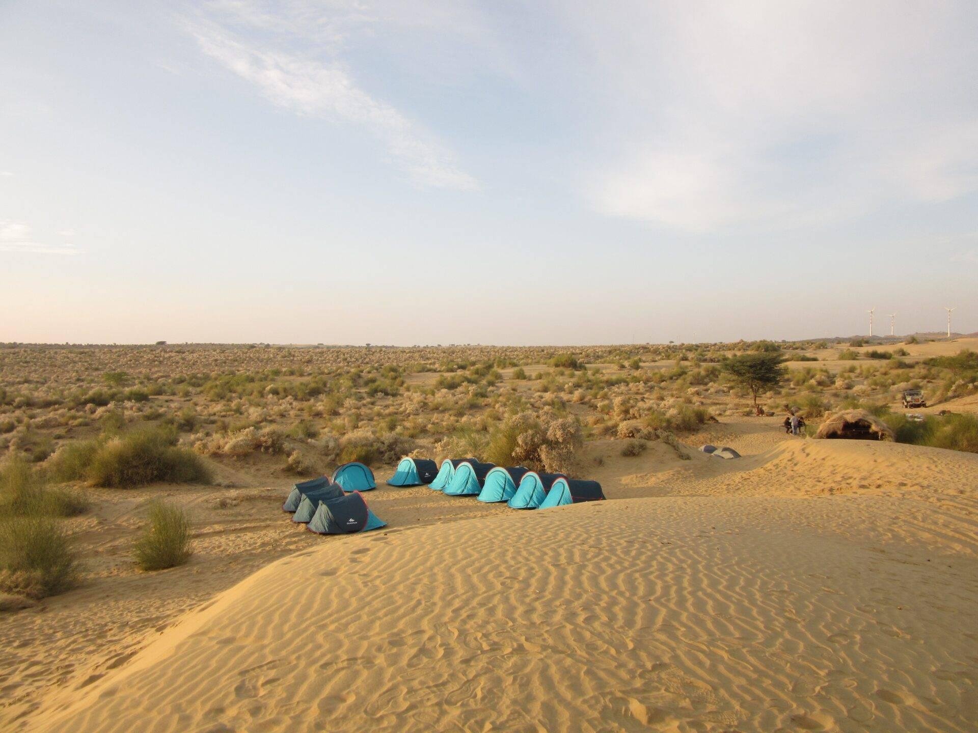 Accampamento di tende blu nel deserto del Rajasthan con dune di sabbia e vegetazione rada