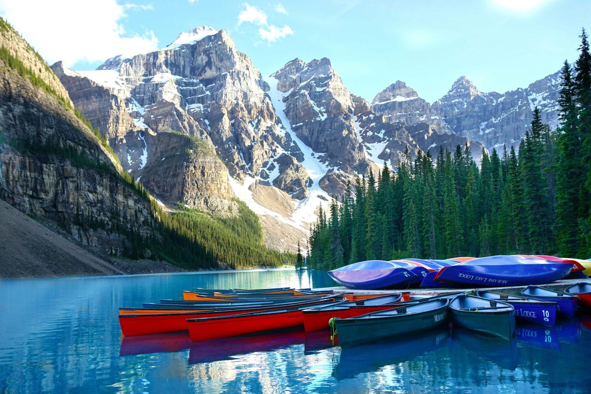 Canoe colorate allineate su un lago turchese incorniciato da montagne rocciose innevate e foreste di conifere