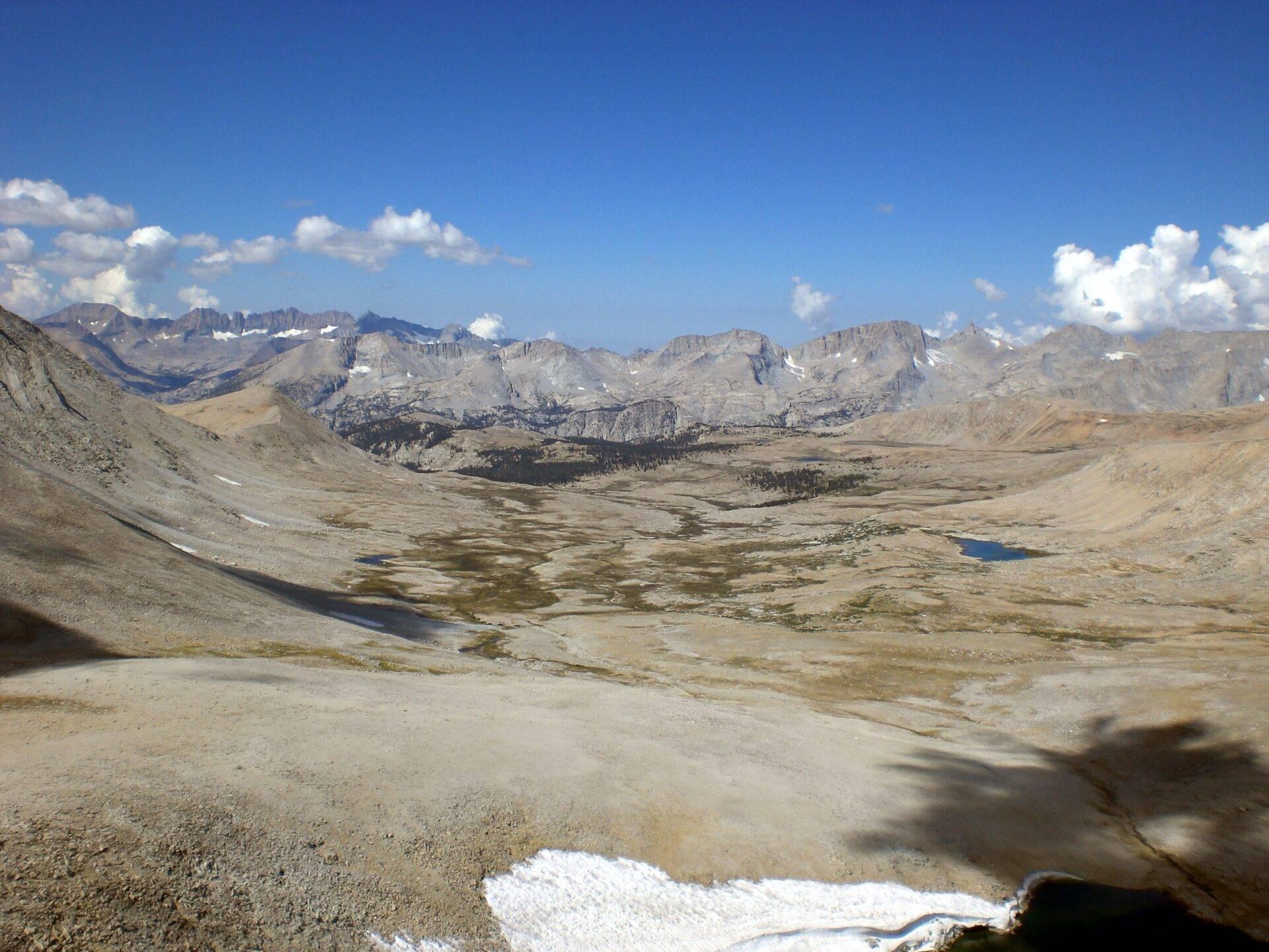 Vista panorámica de un valle alpino desértico con lagos glaciares, picos rocosos y nieve residual