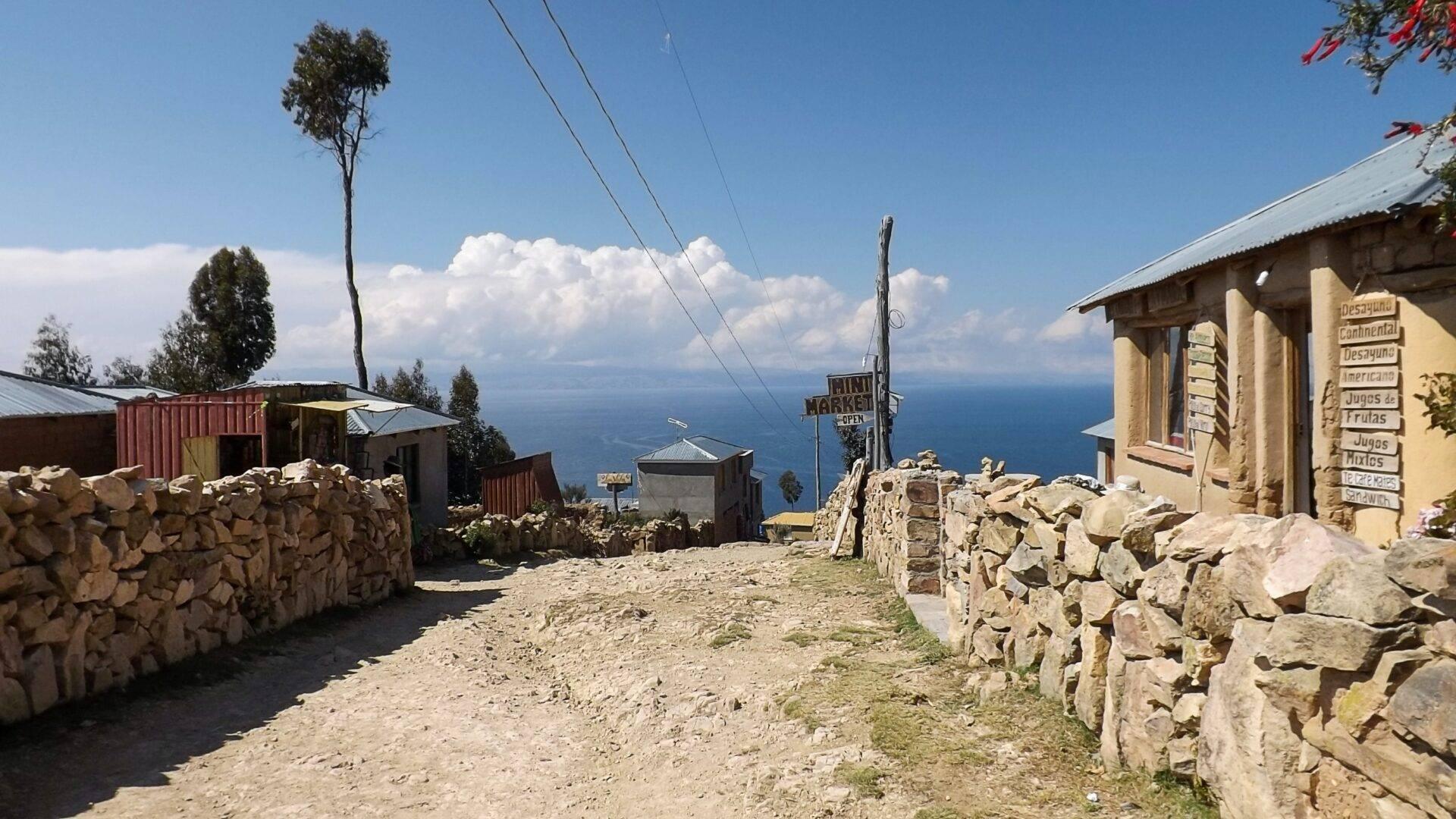 Un piccolo villaggio di montagna ad alta quota con case in pietra, muretti a secco e vista su un lago sottostante