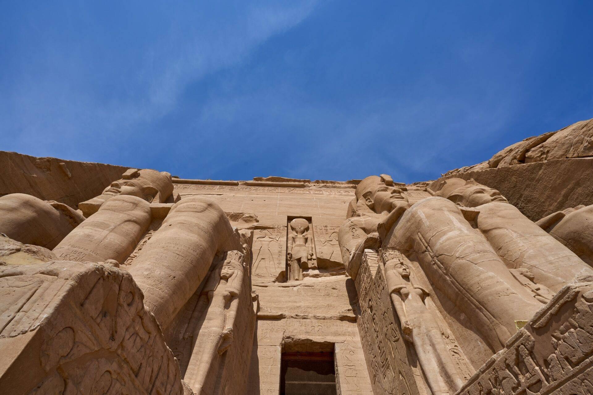 Facciata monumentale di un antico tempio egizio con colossi scolpiti e geroglifici sotto un cielo azzurro