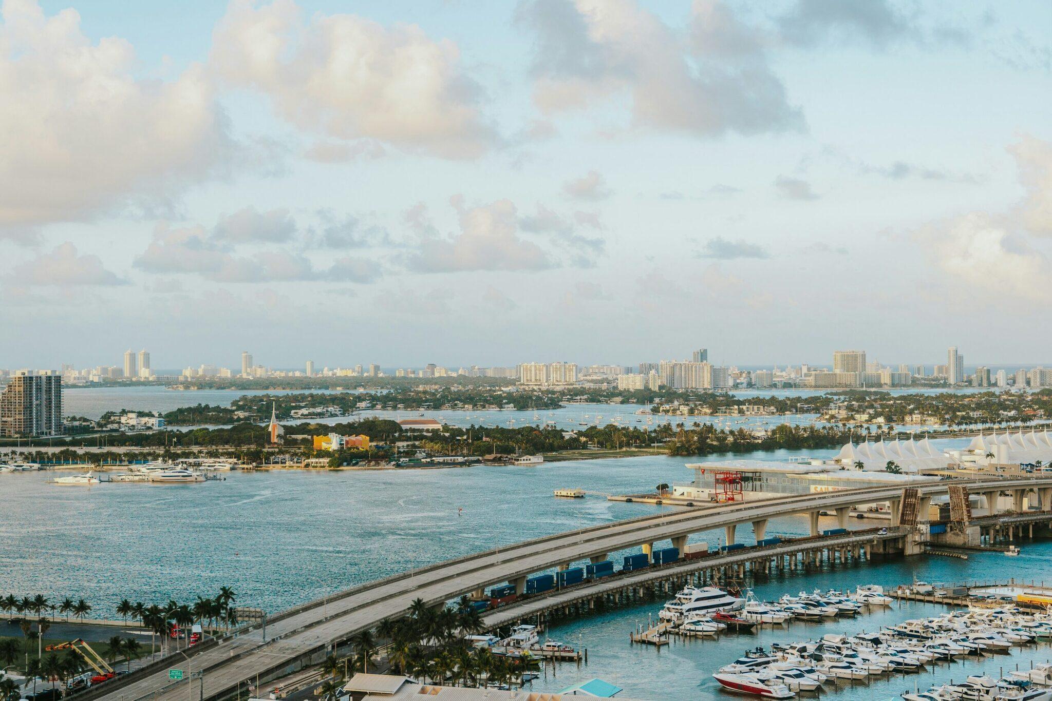 Aerial view of a tropical marina with moored boats, a highway bridge and an urban skyline in the background