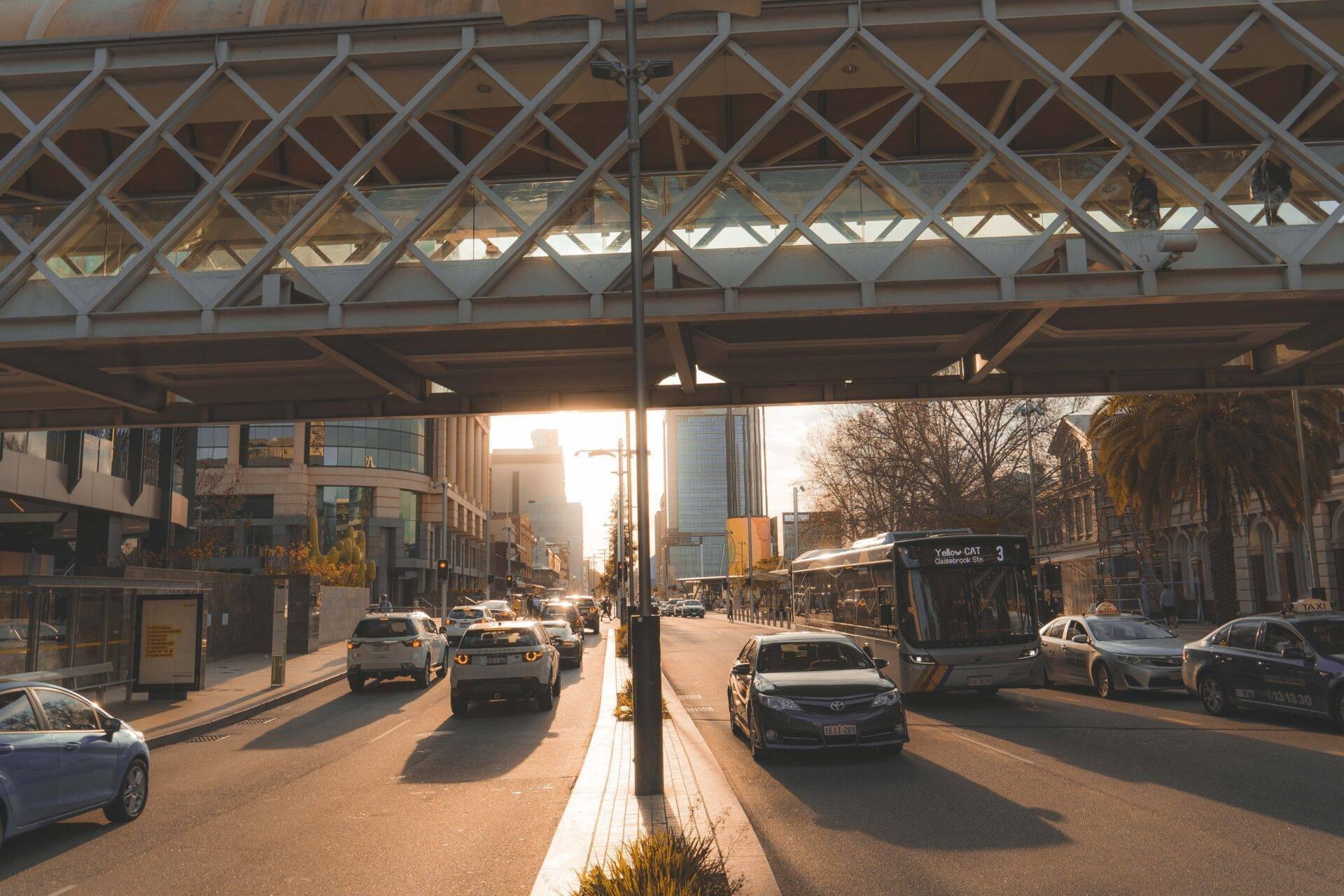 Una strada urbana australiana sotto una struttura in vetro con auto, autobus ed edifici moderni al tramonto