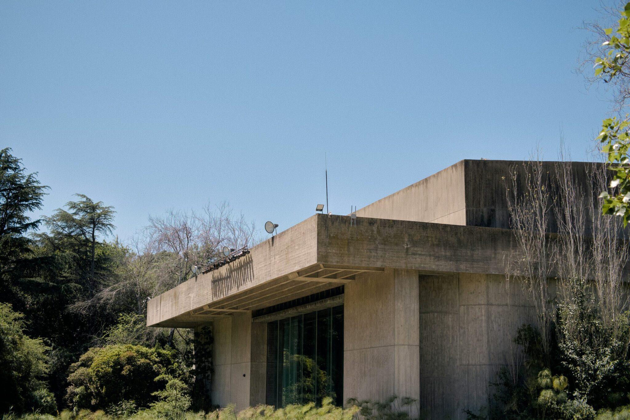Modernes Rohbetongebäude mit überhängendem Dach, umgeben von üppiger Vegetation unter wolkenlosem Himmel