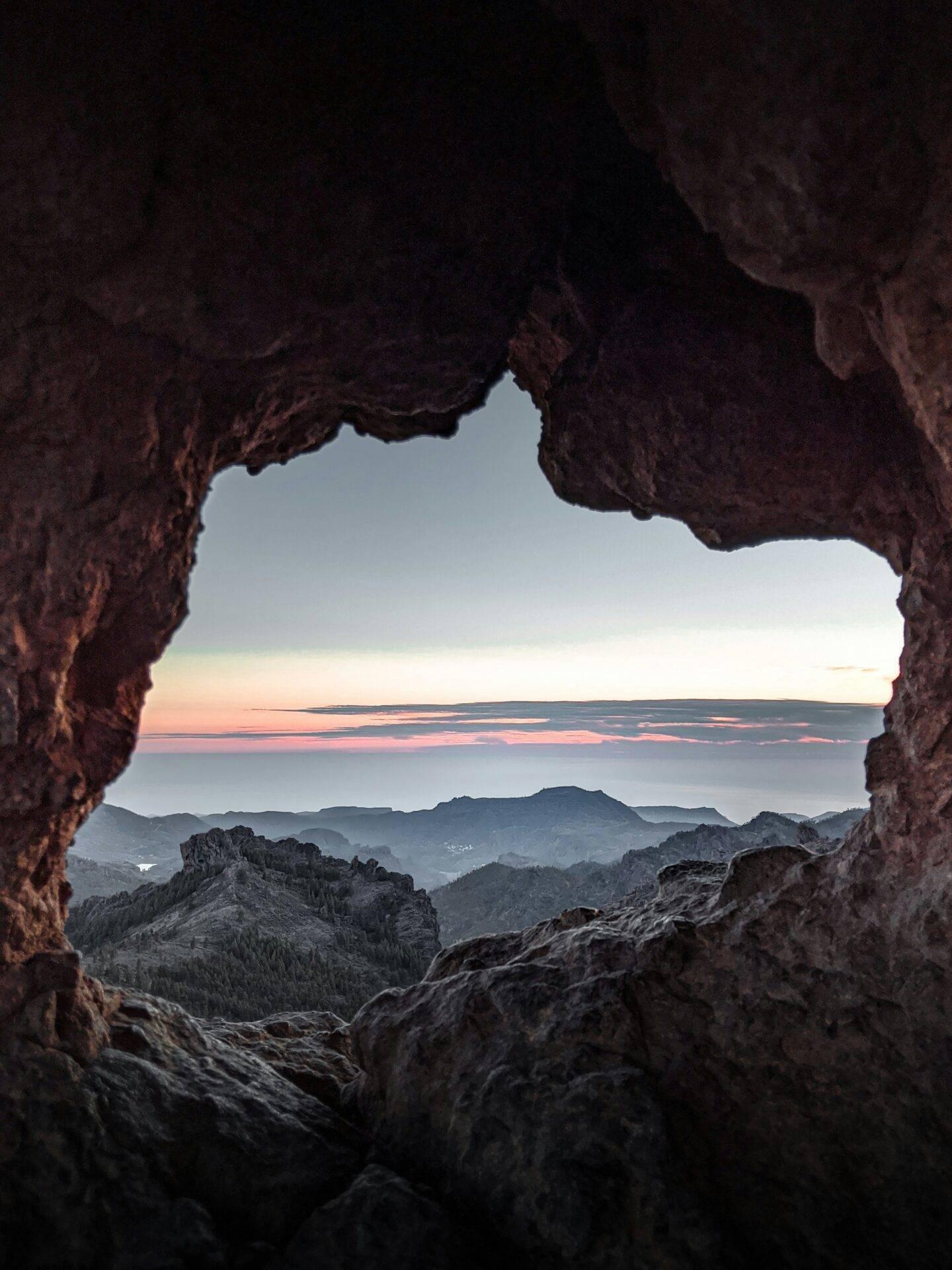 Vue depuis une grotte rocheuse sur un paysage montagneux côtier au coucher du soleil